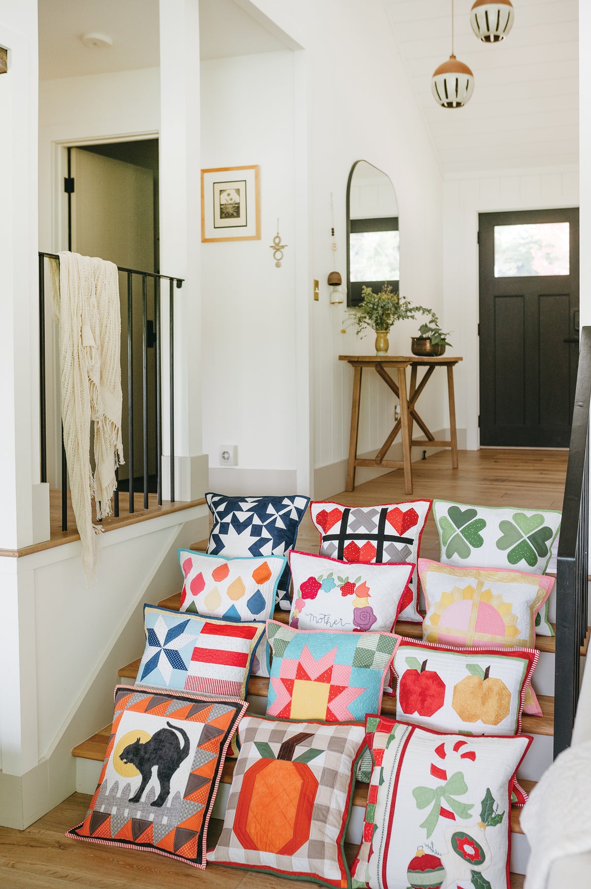 Twelve quilted pillow projects from Sew a Pillow a Month with seasonal and patterned designs arranged on a staircase.
