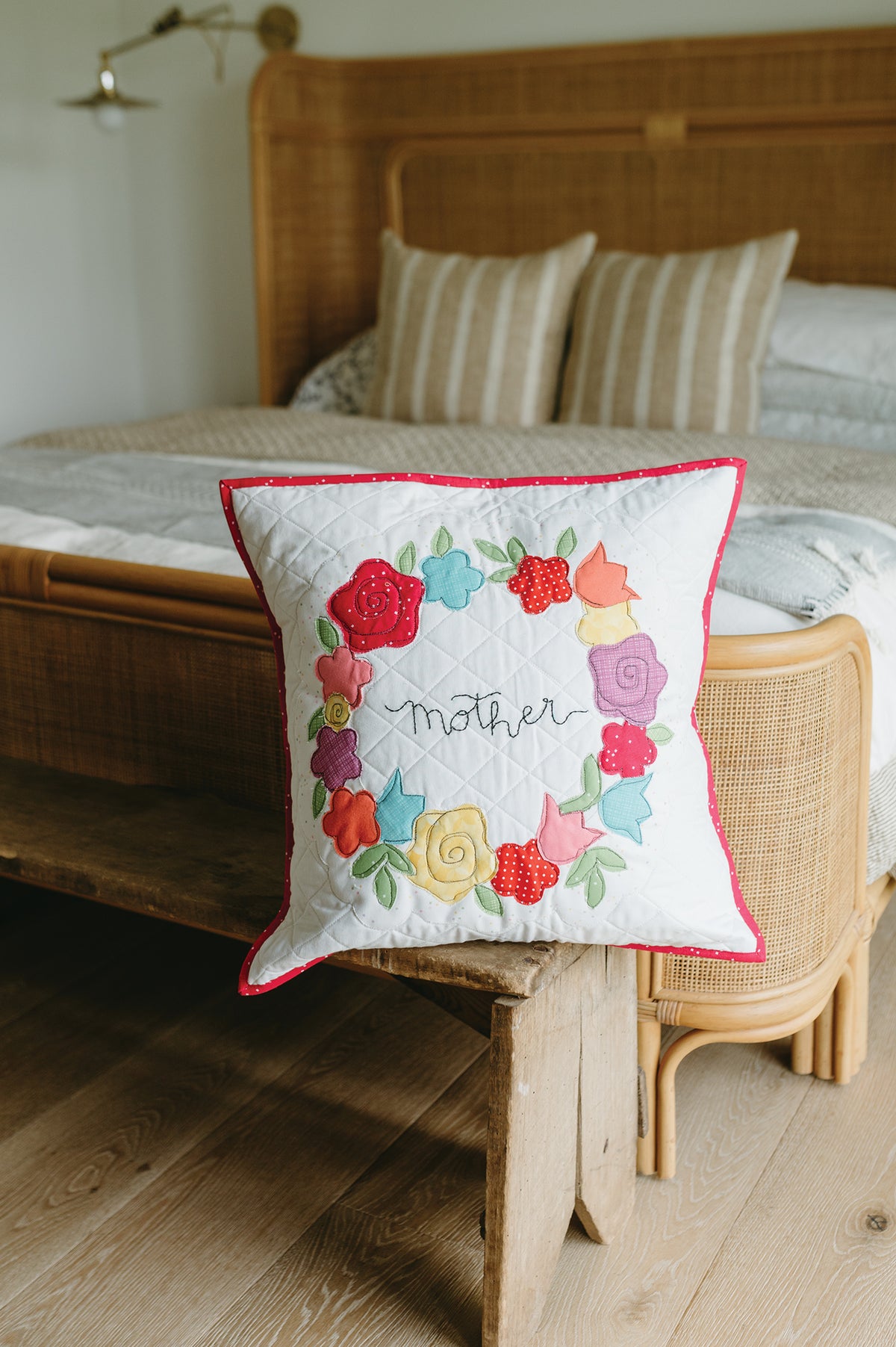 A white quilted throw pillow from Sew a Month featuring a colorful fabric floral wreath surrounding the embroidered word mother, perfect for seasonal decorating.