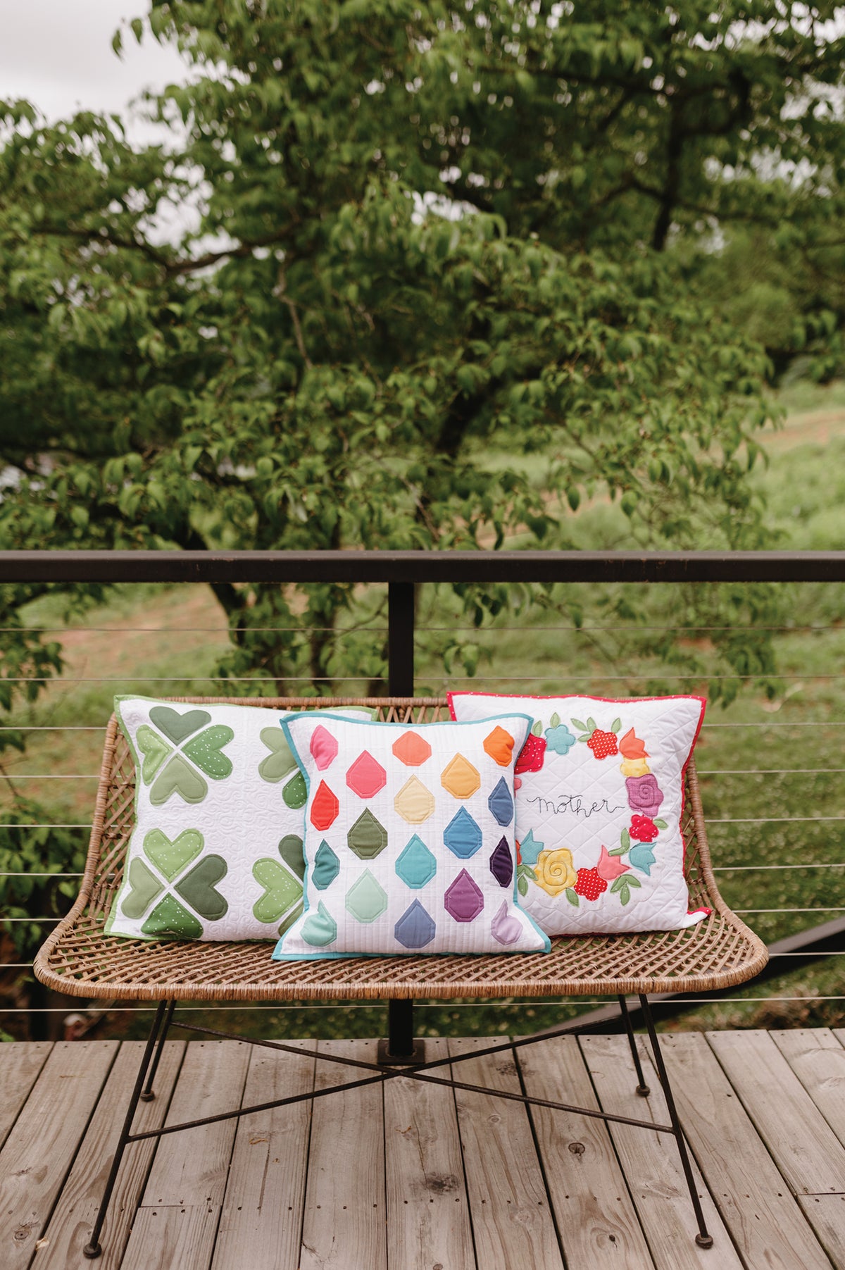 Three Sew a Pillow a Month decorative pillows by C&T Publishing, featuring shamrock, raindrop, and floral wreath patterns, arranged on a wicker patio chair.