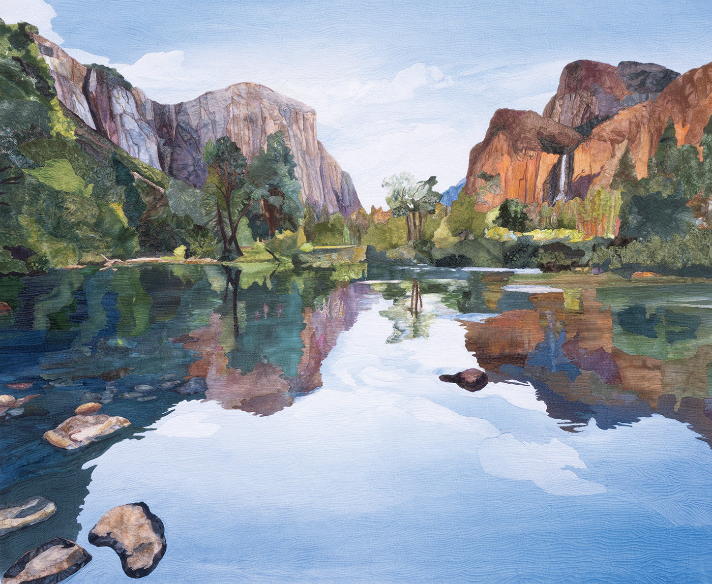 A serene river reflects rocky cliffs and trees beneath a blue sky, with green foliage and stones lining the water’s edge—a peaceful scene captured in quilt realism. “Quilted Realism” by C&T Publishing brings natural beauty to life, blending photo-to-quilt artistry to evoke the impression of an art quilt transformed into reality.