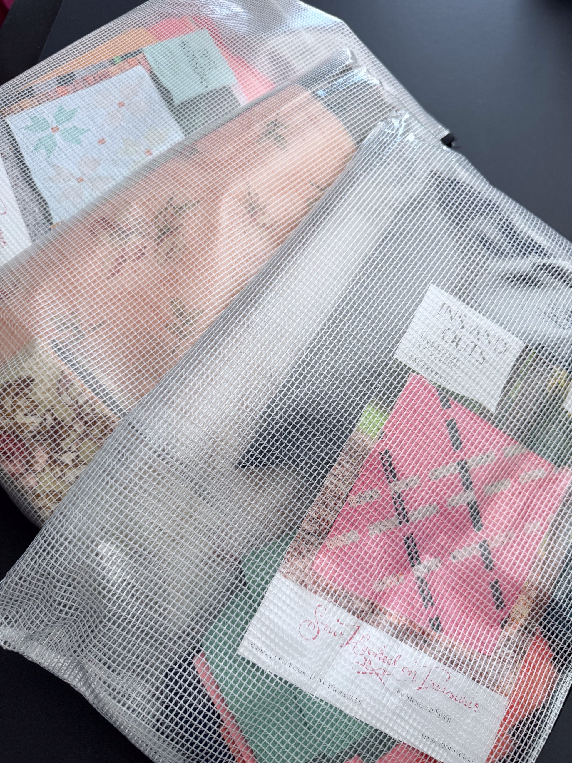 Two mesh zipper bags accompany "Organize Your Creative Space: A Step-by-Step Craft Room Reset" by Creative Spark, displayed on a black surface. Filled with colorful papers, cards, and notebooks that are partially visible through the semi-transparent material, these bags are ideal for sewing supplies storage or quilting organization.