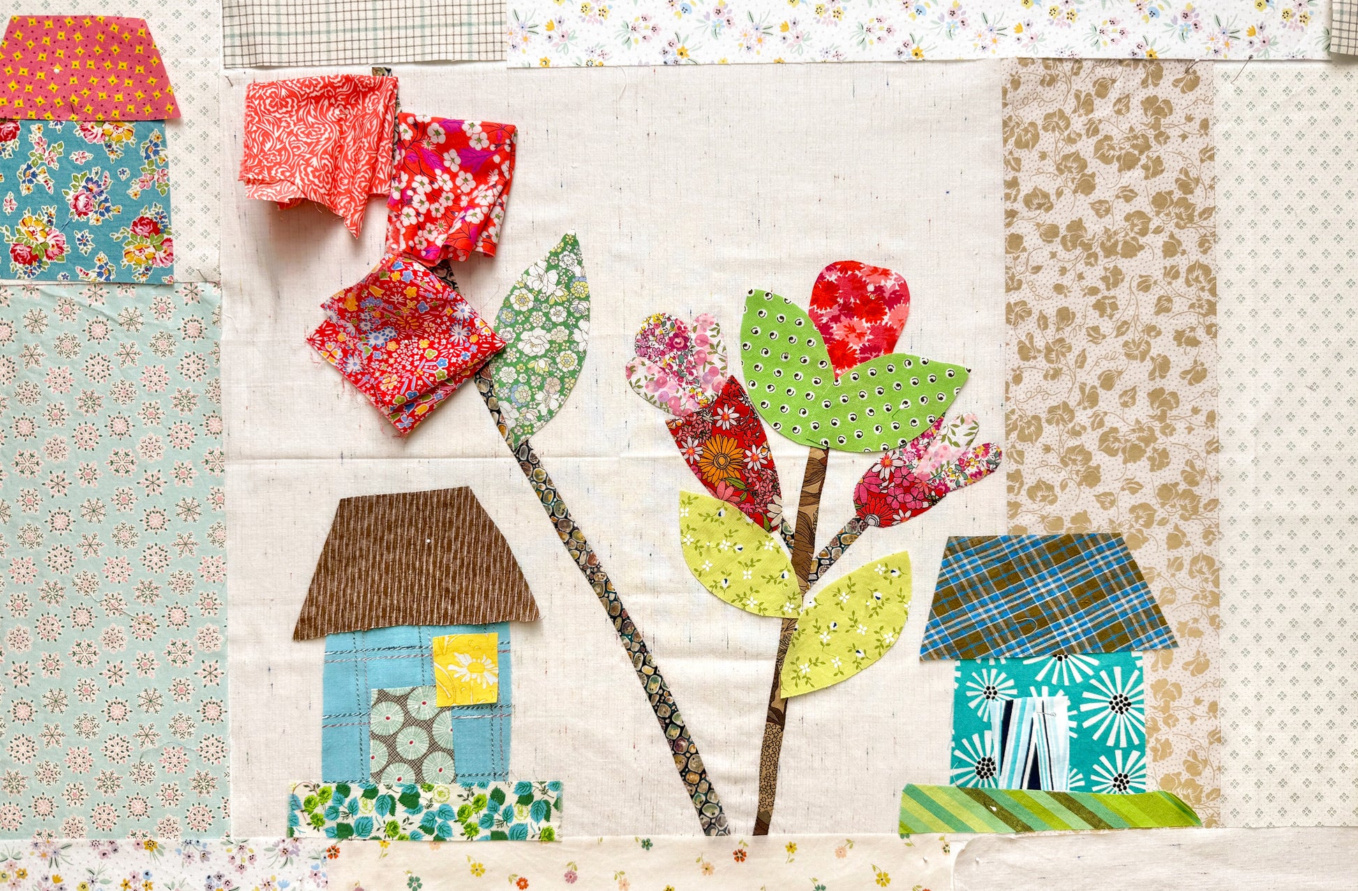 The Buttonwood Village: Build an Adventure Block of the Month by Creative Spark features a colorful quilt with whimsical houses, flowers, and leaves on a light background—perfect for any appliqué project.