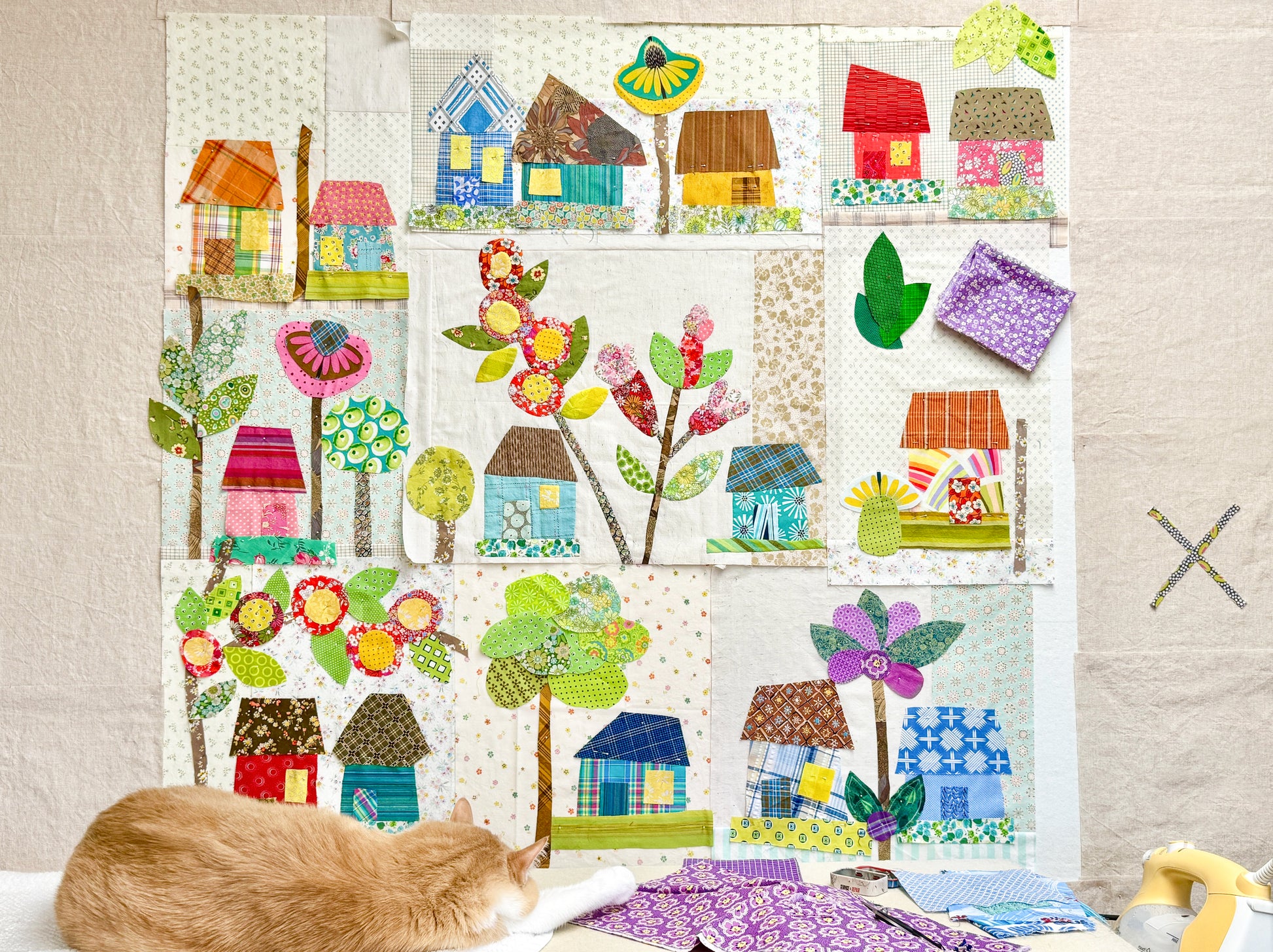 A cat rests on a wall with a quilt among charming houses—Buttonwood Village: Build an Adventure Block of the Month by Creative Spark is ideal inspiration for your next appliqué or BOM course project.