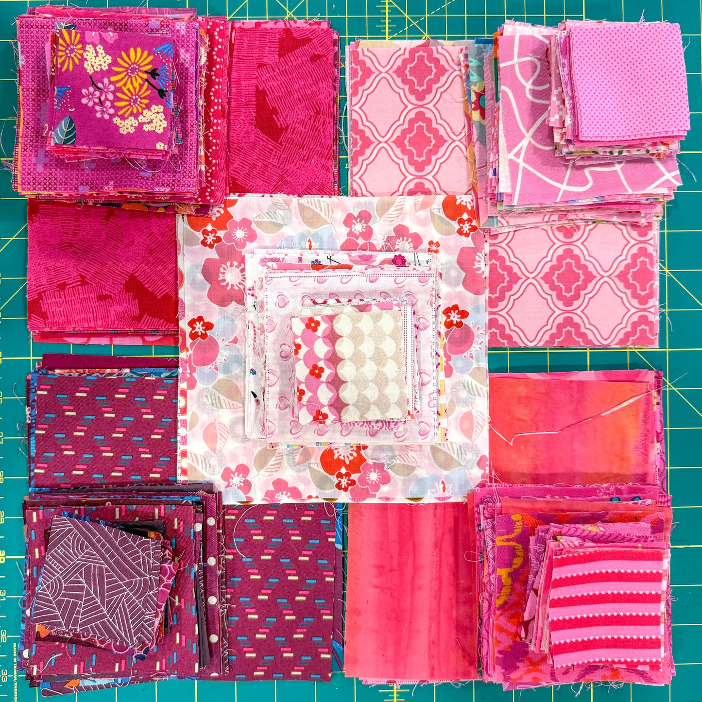 Neatly stacked pink, red, and purple fabric squares on a green cutting mat demonstrate value-based color choices—perfect for design inspiration from Creative Spark’s "The Misunderstood Quilt: Blend Color, Value & Precision.