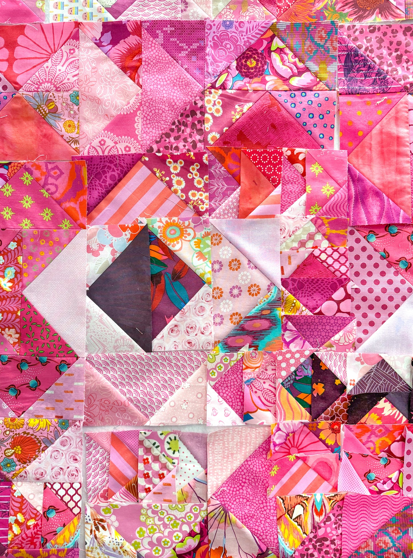 The Misunderstood Quilt by Creative Spark features a blend of pink, red, and purple fabrics in a precise patchwork design, showcasing vibrant prints and expert craftsmanship.