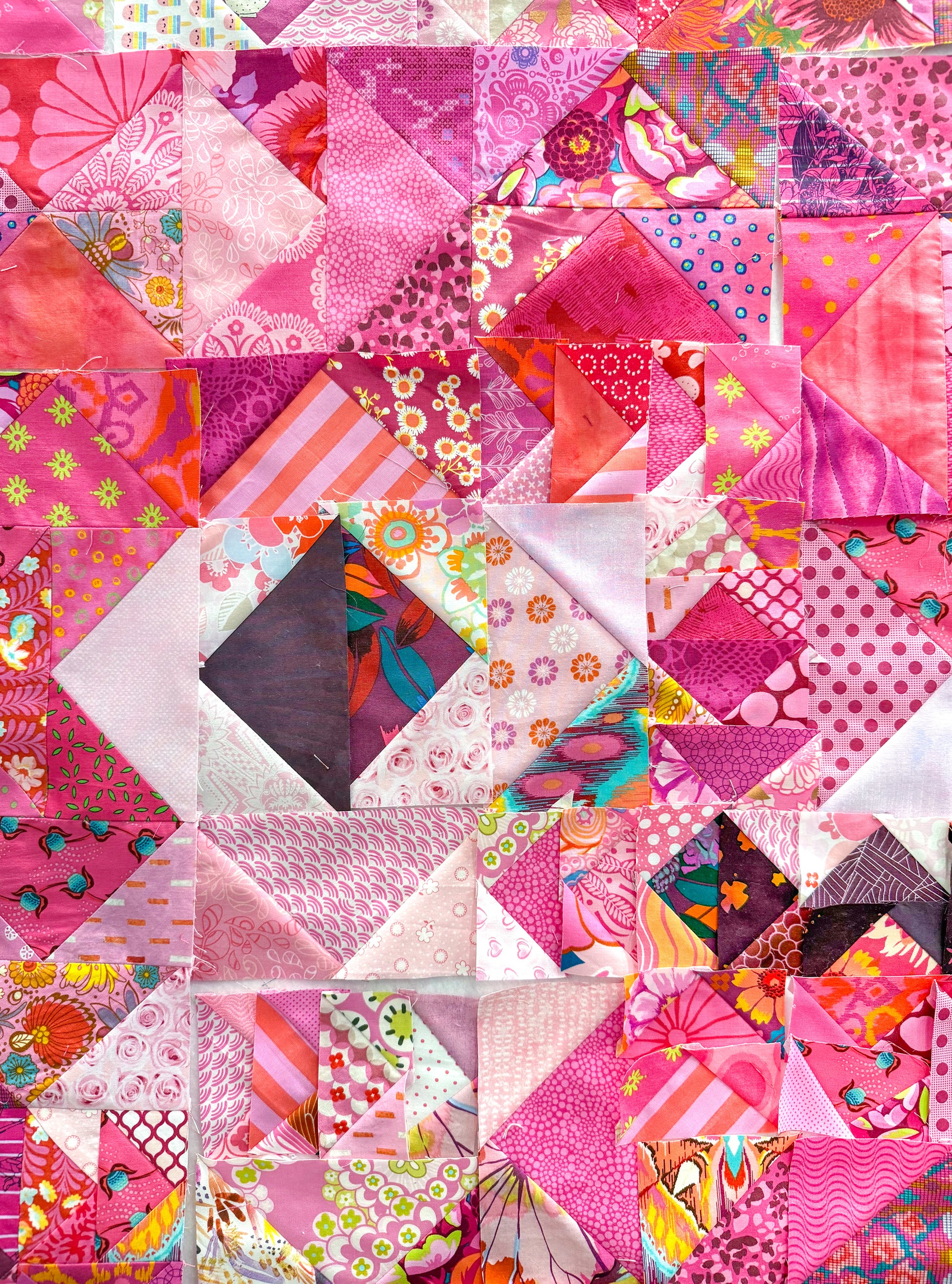 The Misunderstood Quilt by Creative Spark features a blend of pink, red, and purple fabrics in a precise patchwork design, showcasing vibrant prints and expert craftsmanship.
