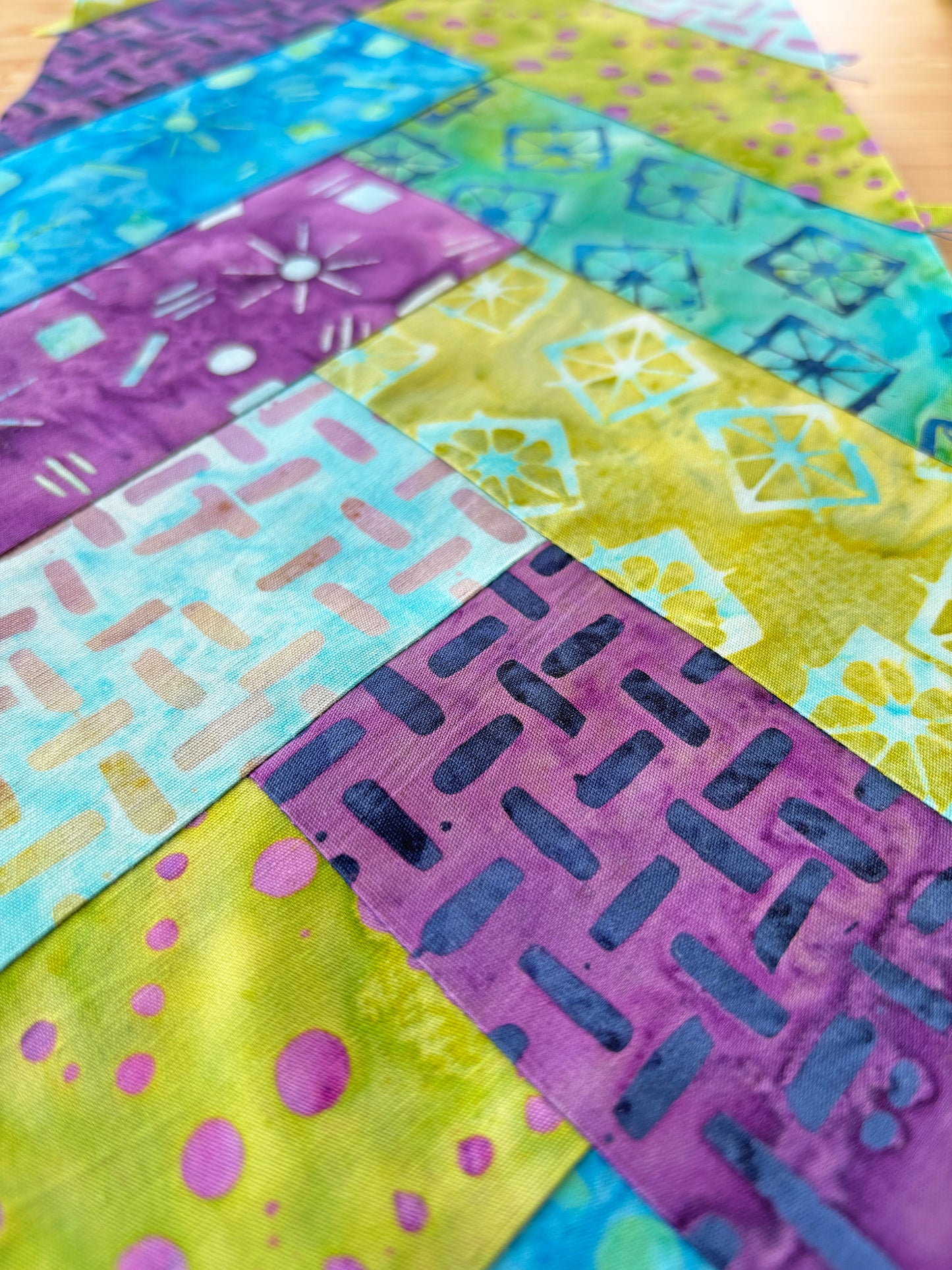 Close-up of a vibrant quilt with rectangular patches in purple, blue, green, and yellow, arranged diagonally. Find inspiration for your own projects with Patchwork Braids 101 Basics by Creative Spark.