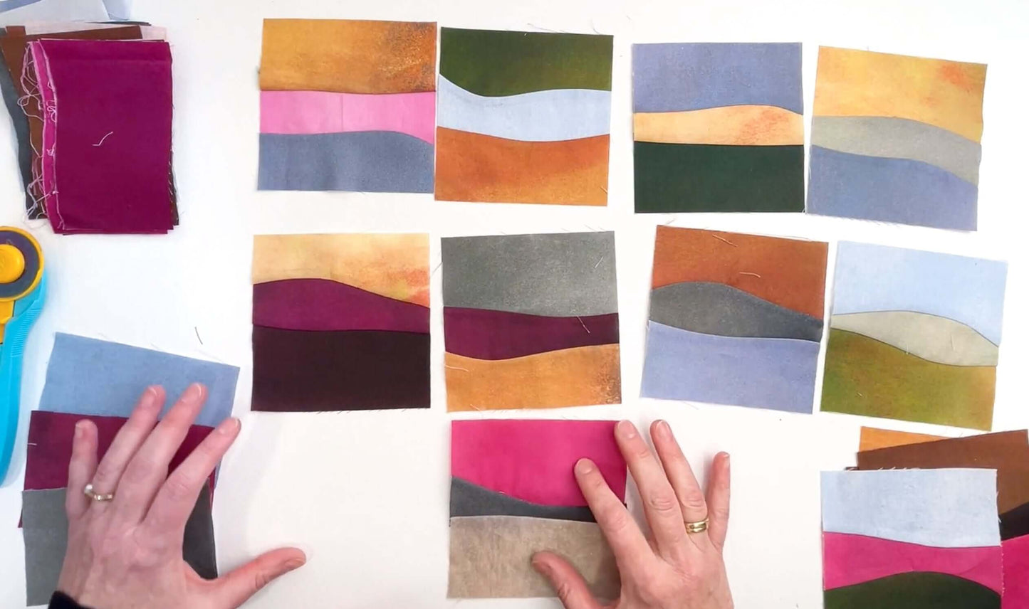 A person arranges vibrant fabric squares with abstract, wavy designs—ideal for scenic quilts or improv landscapes using Creative Spark's Landscapes as Building Blocks: Quilt the Places You Love with Easy Improv. Stacks of fabric and a rotary cutter sit to the left.