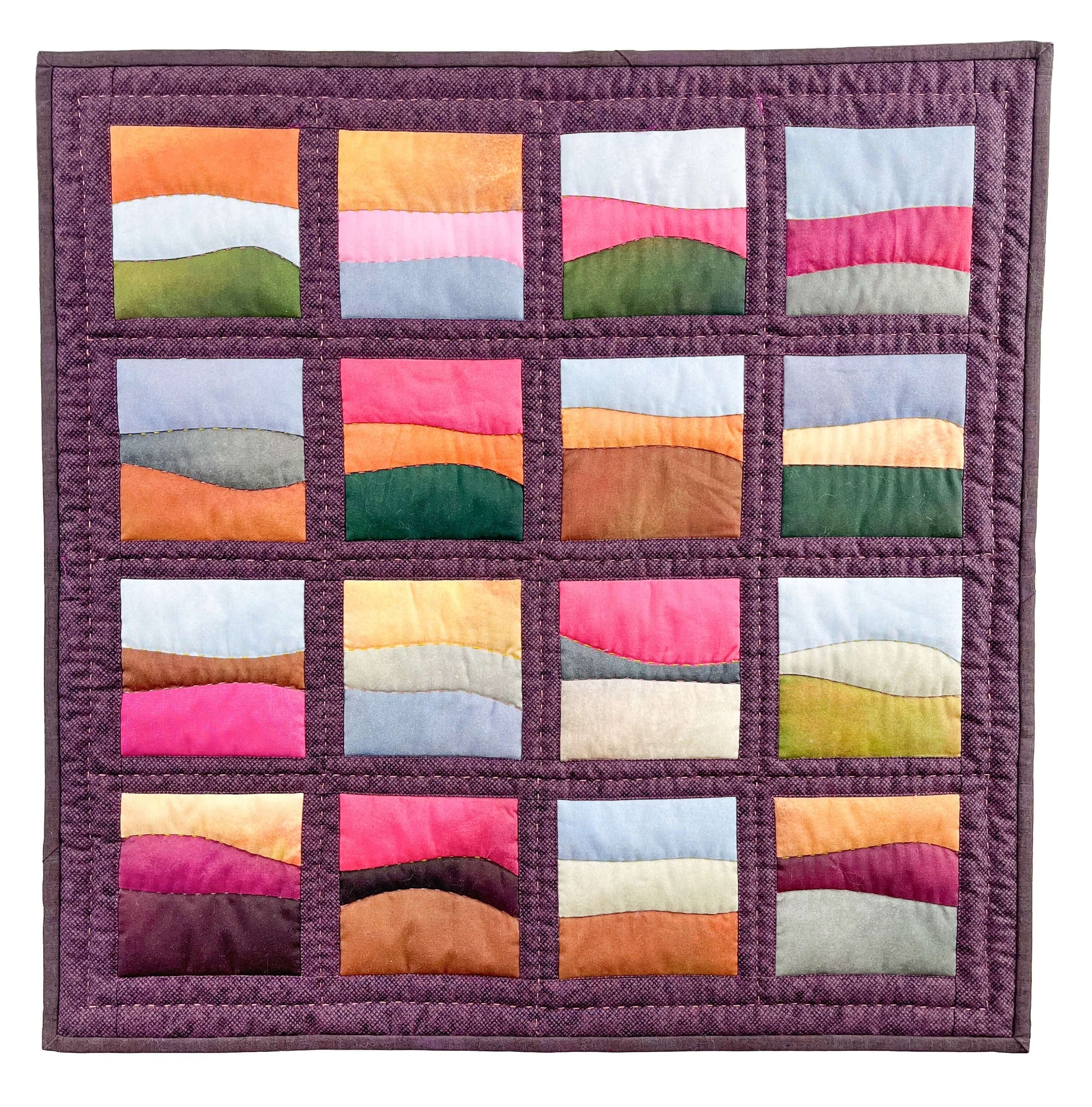 The "Landscapes as Building Blocks: Quilt the Places You Love with Easy Improv" kit by Creative Spark features 16 vibrant, wavy landscape blocks in pink, orange, green, brown, purple, and blue—ideal for scenic quilt enthusiasts.