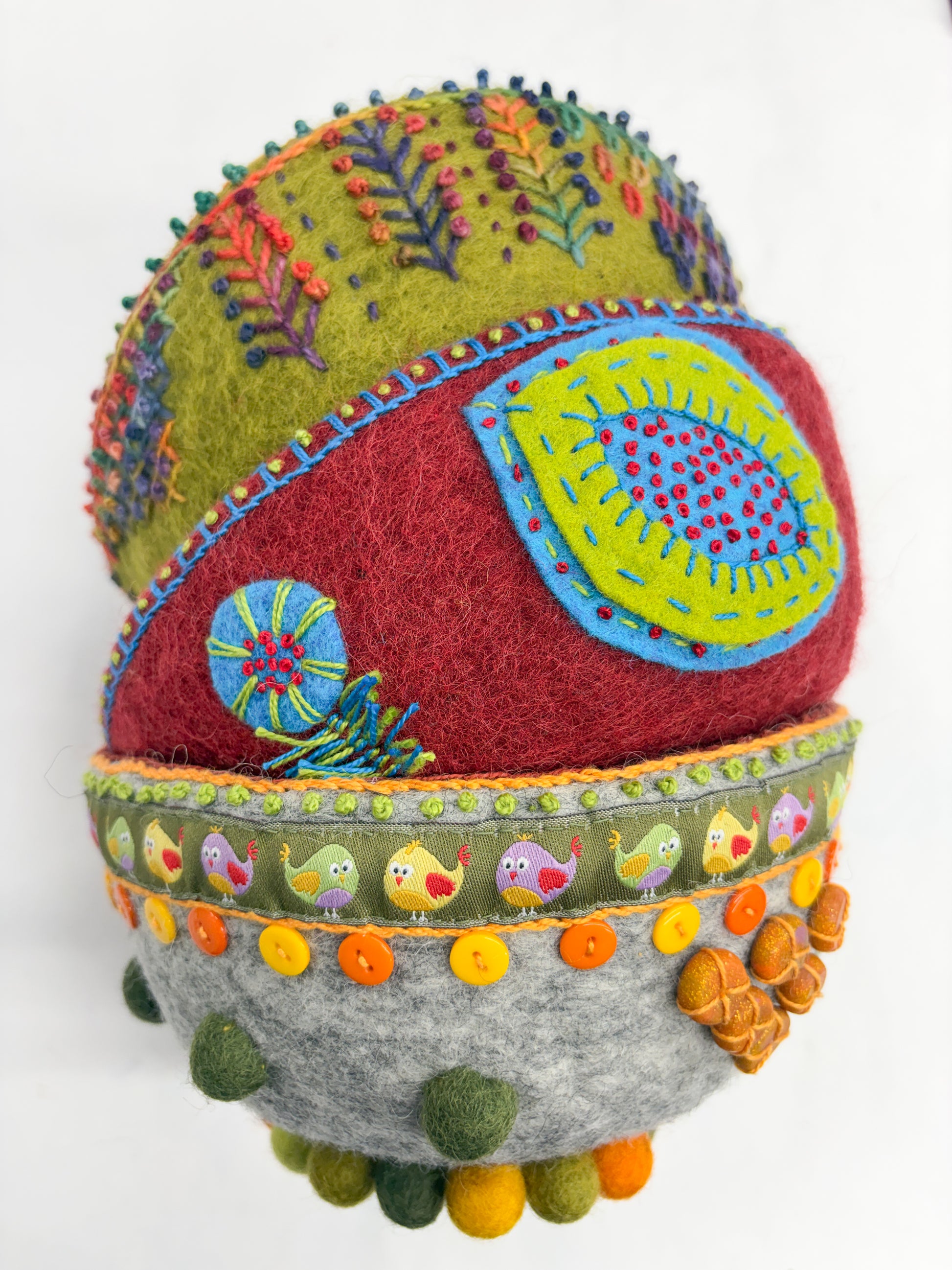 Embroidery in the Round by Creative Spark is a vibrant oval felt bowl adorned with embroidery, appliqué, felted wool, buttons, and a cartoon bird ribbon, displayed on a white background.