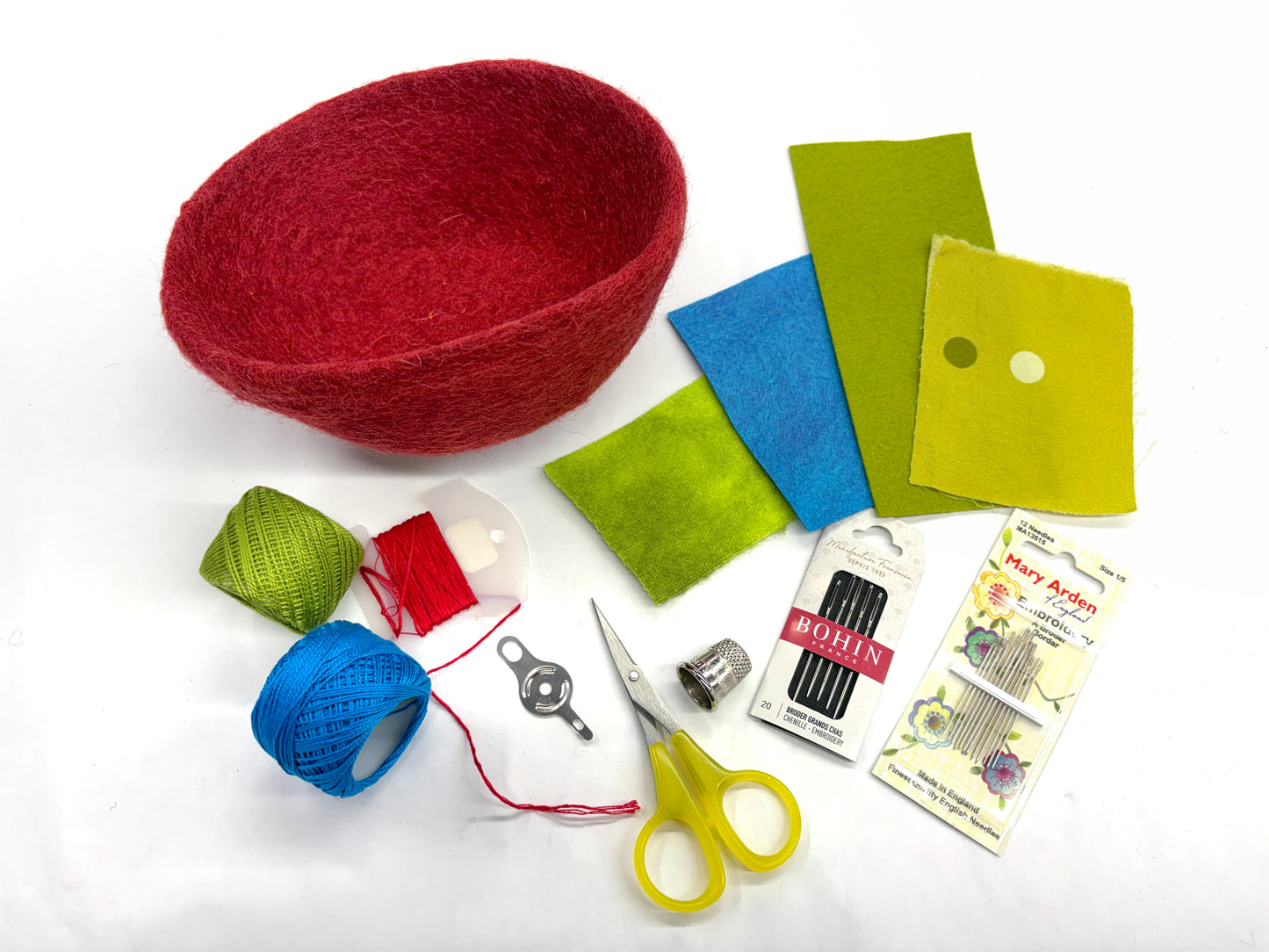 The Creative Spark "Embroidery in the Round: Learn Stitching & Embellishment on Felt Bowls" kit features a red felt bowl, colorful felt pieces, thread, needles, thimble, yellow scissors, and more—ideal for embroidery or appliqué projects.