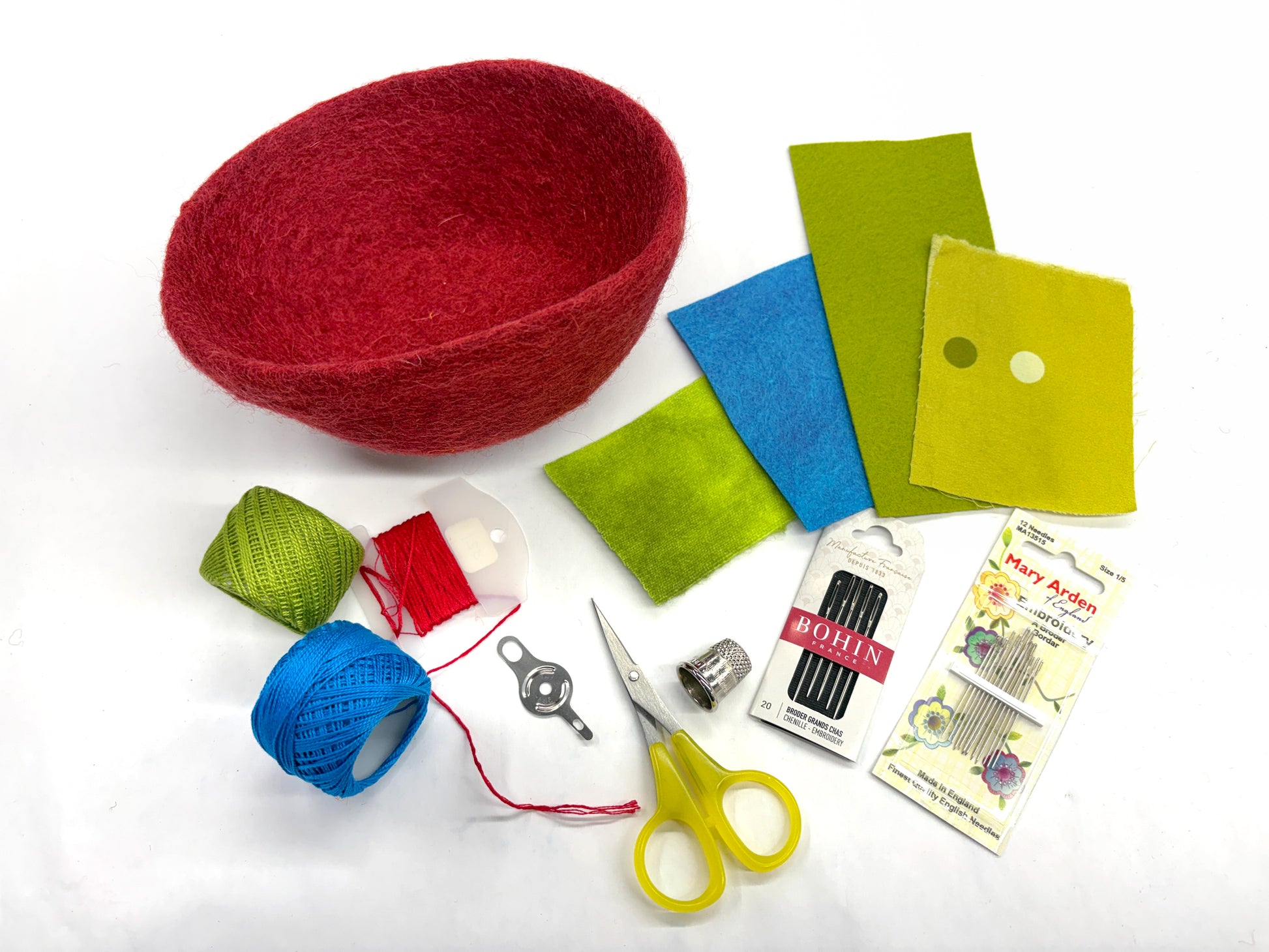 The Creative Spark "Embroidery in the Round: Learn Stitching & Embellishment on Felt Bowls" kit features a red felt bowl, colorful felt pieces, thread, needles, thimble, yellow scissors, and more—ideal for embroidery or appliqué projects.