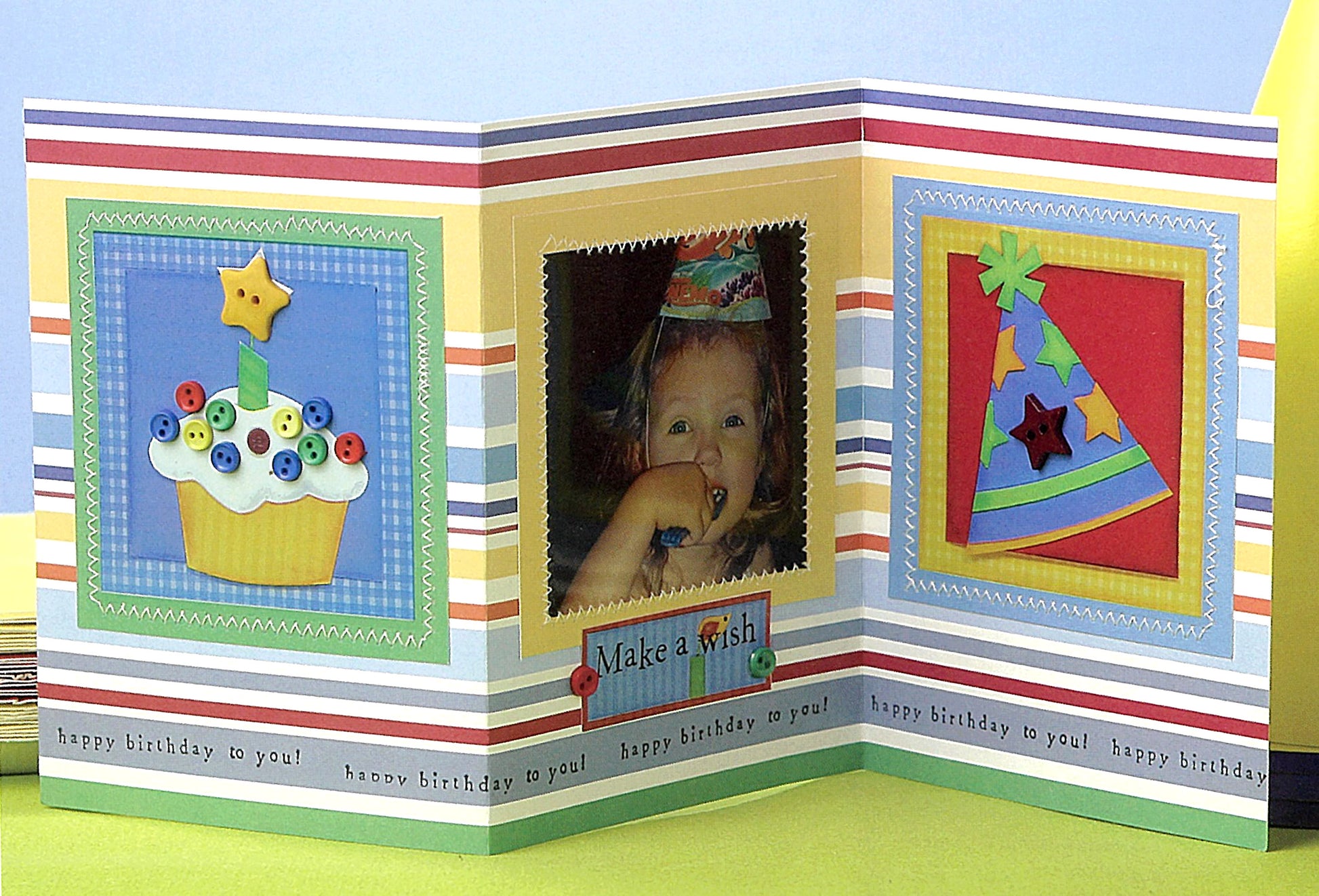 A colorful, tri-fold birthday card from Leisure Arts’ The Ultimate Paper Crafts Collection shows a cupcake, happy child with “Make a wish” caption, party hat, striped borders, and “happy birthday to you!”—perfect for paper crafts fans.
