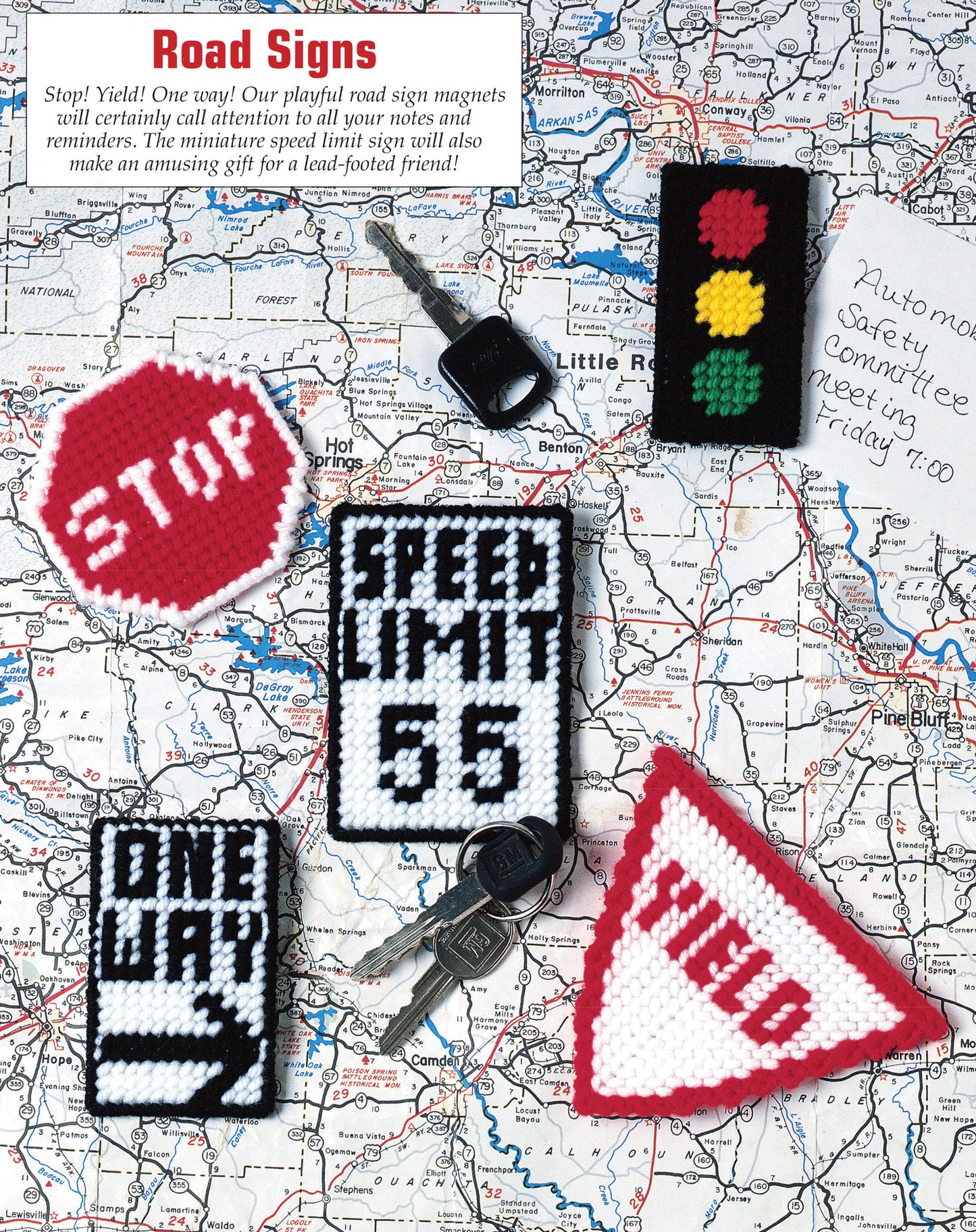 The image features keys, a handwritten note, and five handmade plastic canvas road sign magnets from Leisure Arts’ "300+ Magnets in Plastic Canvas," including stop, yield, speed limit 65, one way, and traffic light designs.