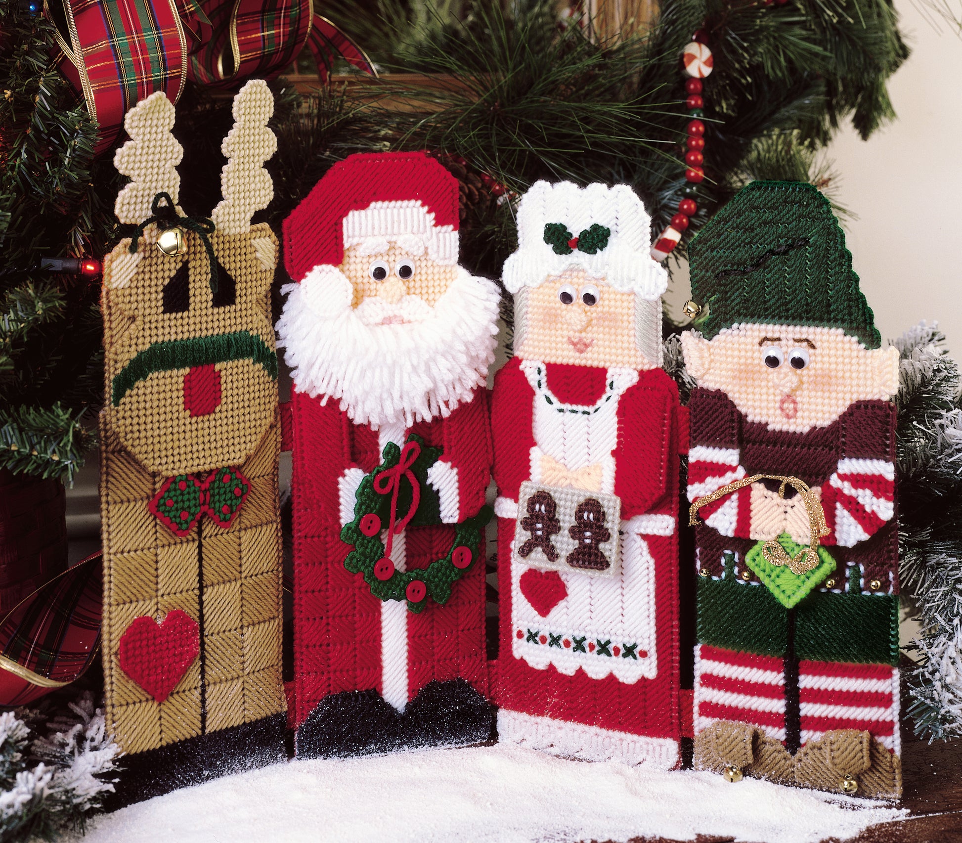 Four festive holiday figures from Leisure Arts’ "Babys Best to Knit and Crochet" make charming beginner projects or baby gift inspiration—featuring a reindeer, Santa, Mrs. Claus, and an elf in front of a Christmas tree.