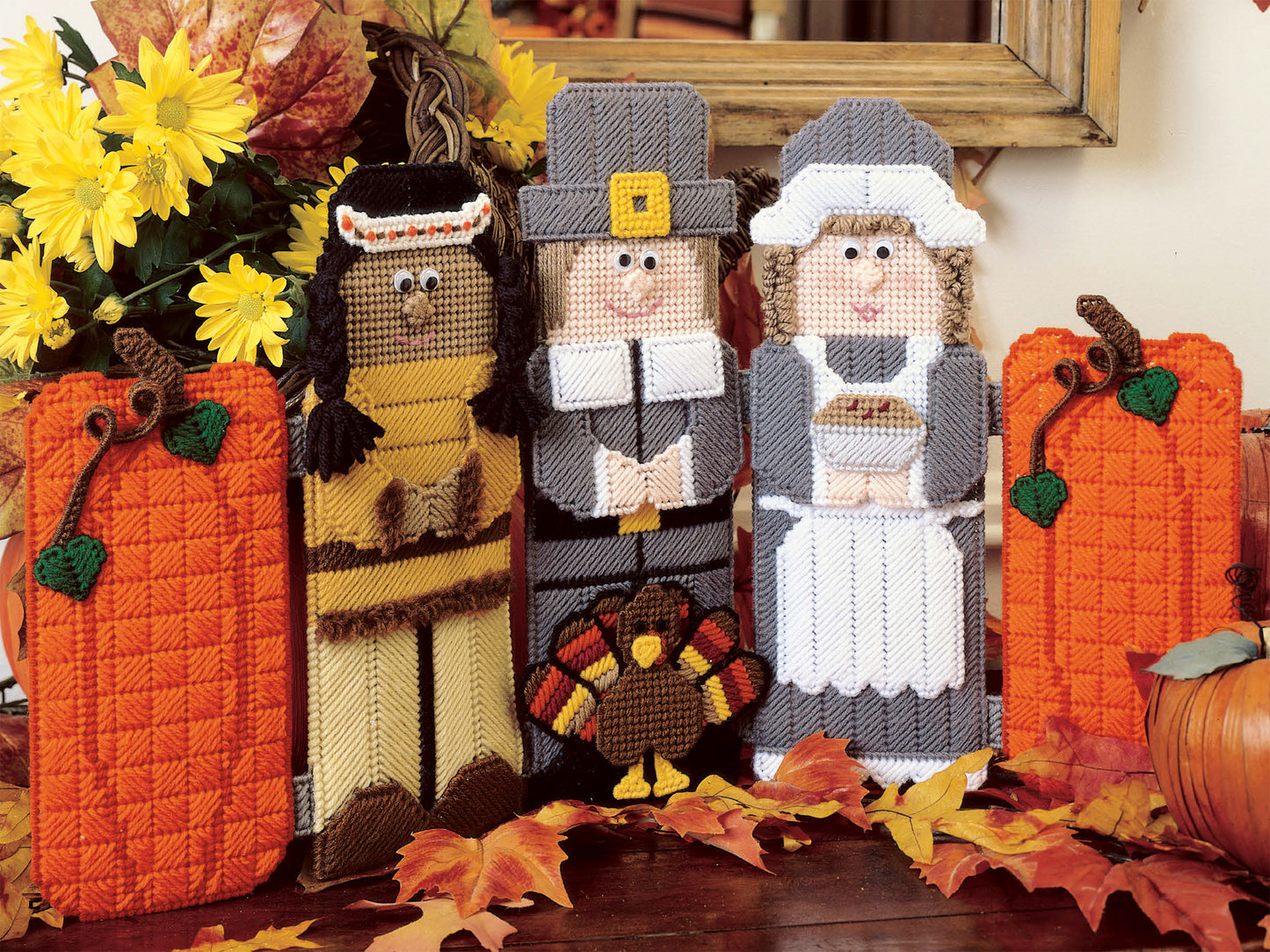Create charming autumn scenes with Babys Best to Knit and Crochet by Leisure Arts, featuring beginner-friendly plastic canvas dolls—a Native American, a Pilgrim man, and a Pilgrim woman—with turkey and pumpkin accents.
