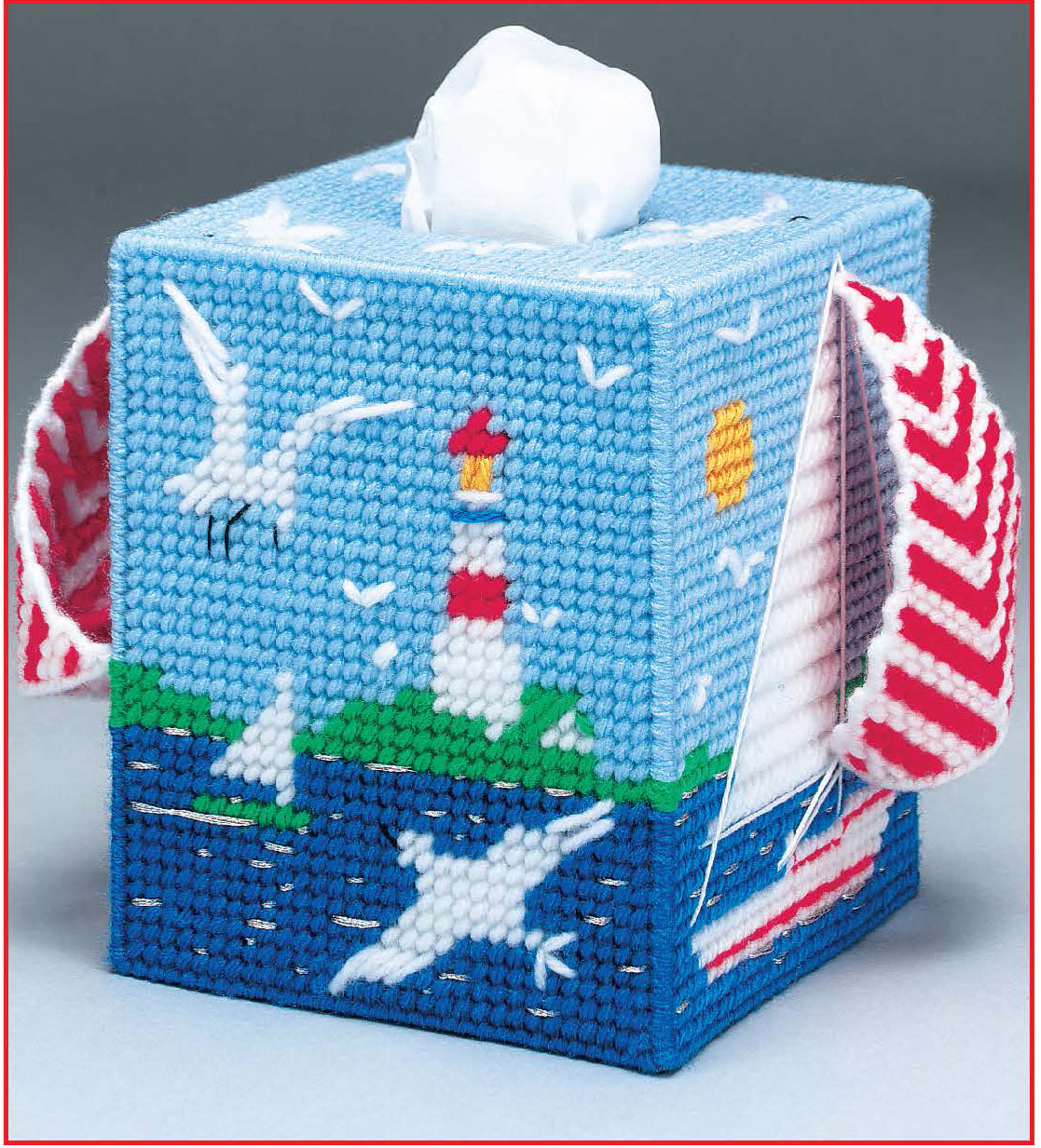 The Leisure Arts Room by Room Plastic Canvas Tissue Box Covers Digital Download features a needlepoint seascape with a lighthouse, seagulls, blue water, and sun—ideal for beginners seeking creative patterns.
