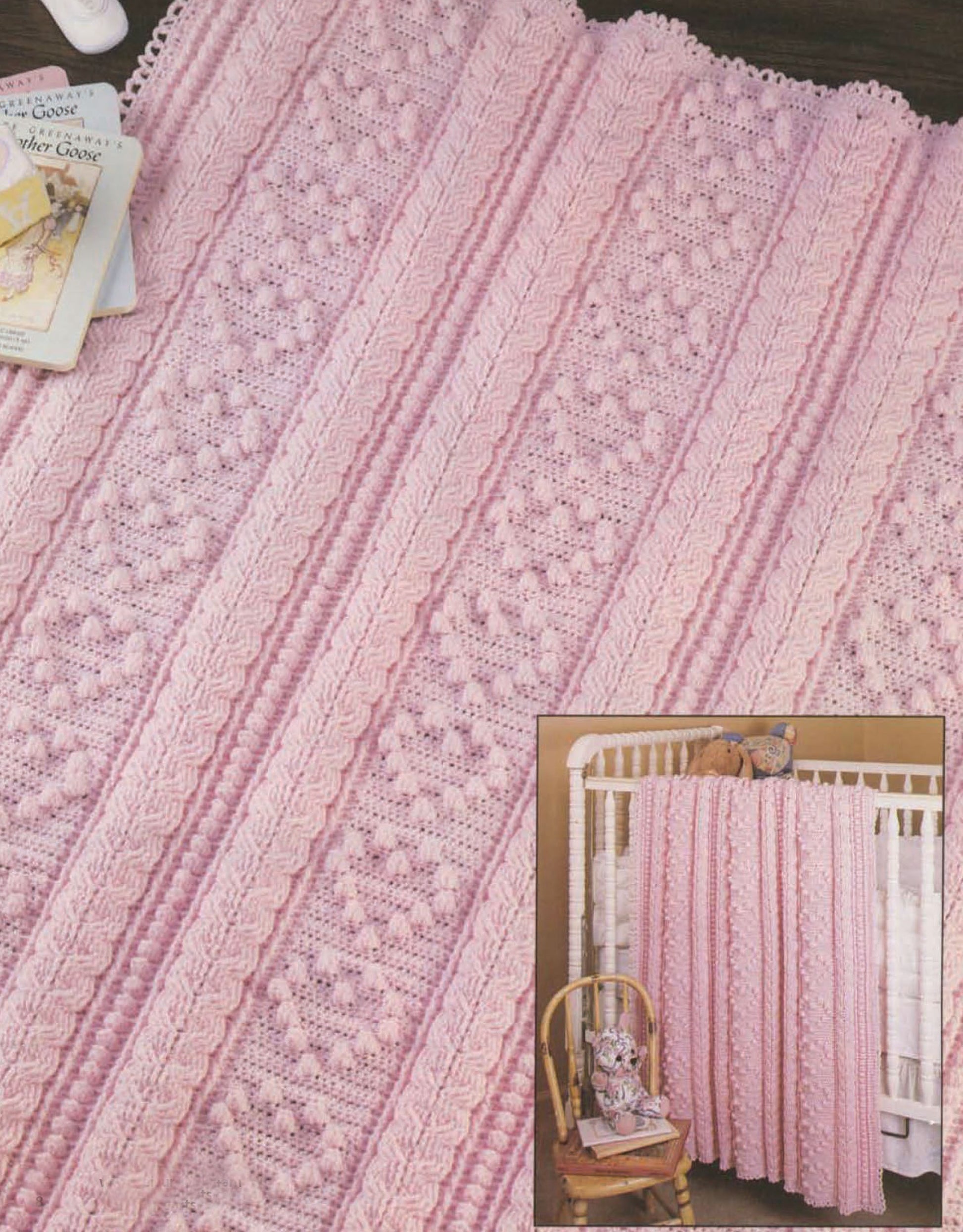 The Aran Baby Afghans Digital Download by Leisure Arts features a soft, light pink sport weight knitted blanket with intricate patterns—shown draped over a white crib beside a doll, perfect inspiration for crochet baby afghans.