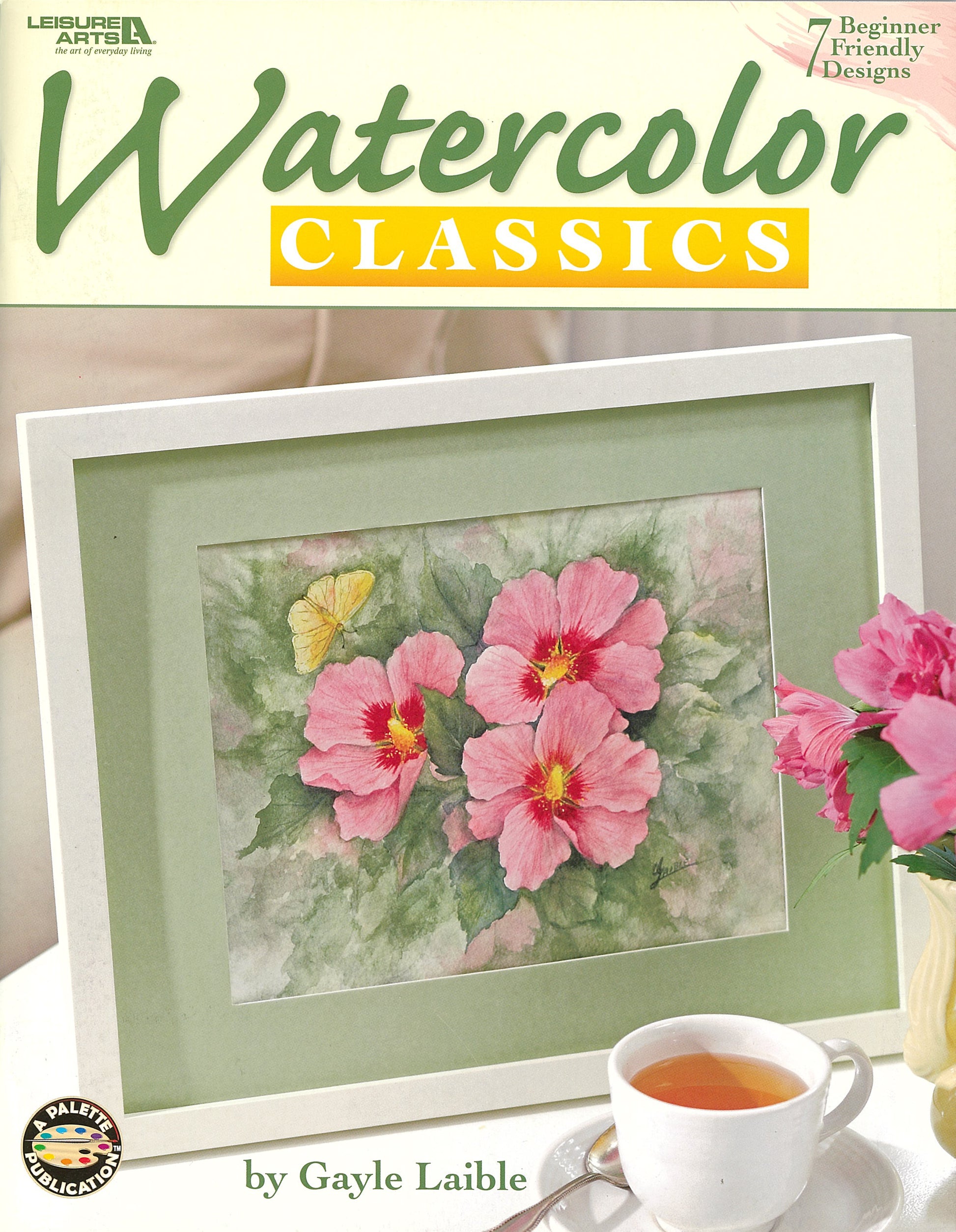 The cover of Leisure Arts’ Watercolor Classics—7 Beginner Friendly Designs features a framed watercolor of pink hibiscus flowers and a butterfly with a cup of tea in front, offering perfect inspiration for beginners.