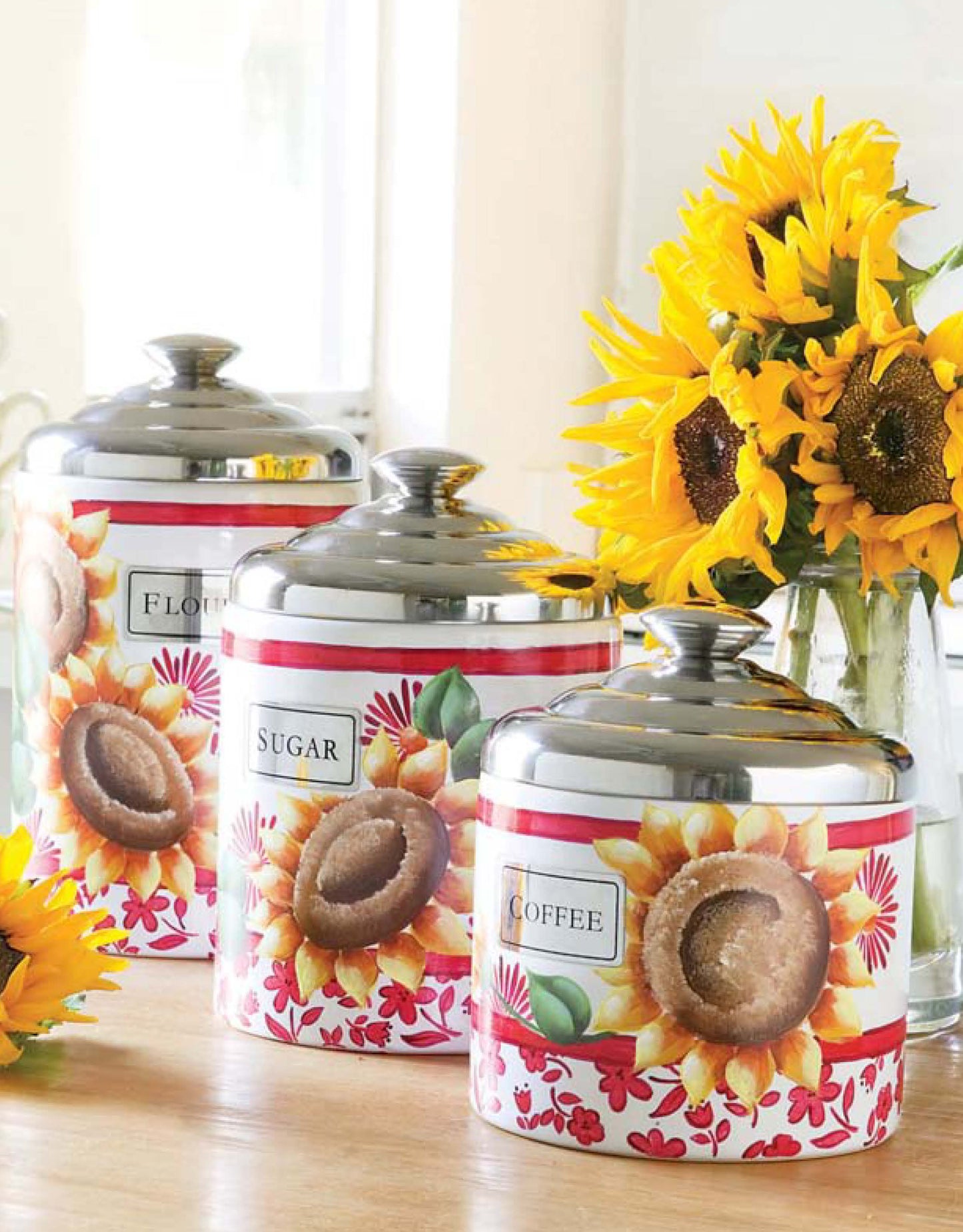 The Painted Kitchen by Leisure Arts features three sunflower-adorned canisters labeled Flour, Sugar, and Coffee. Displayed on a wooden surface with fresh sunflowers, they add cheerful charm and brightness to any kitchen décor.