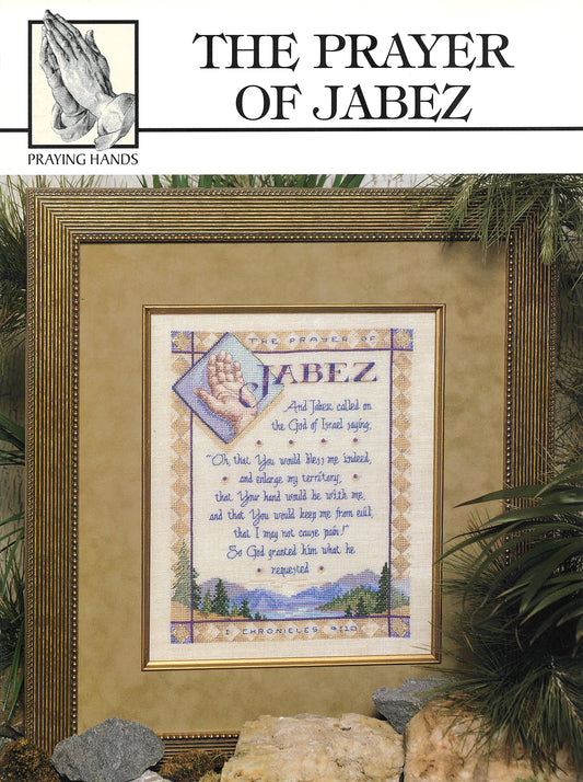 A framed cross-stitch of The Prayer of Jabez by Leisure Arts, with praying hands above the title, surrounded by green plants and rocks. Designed by Elisabeth Parker. Print ISBN available.