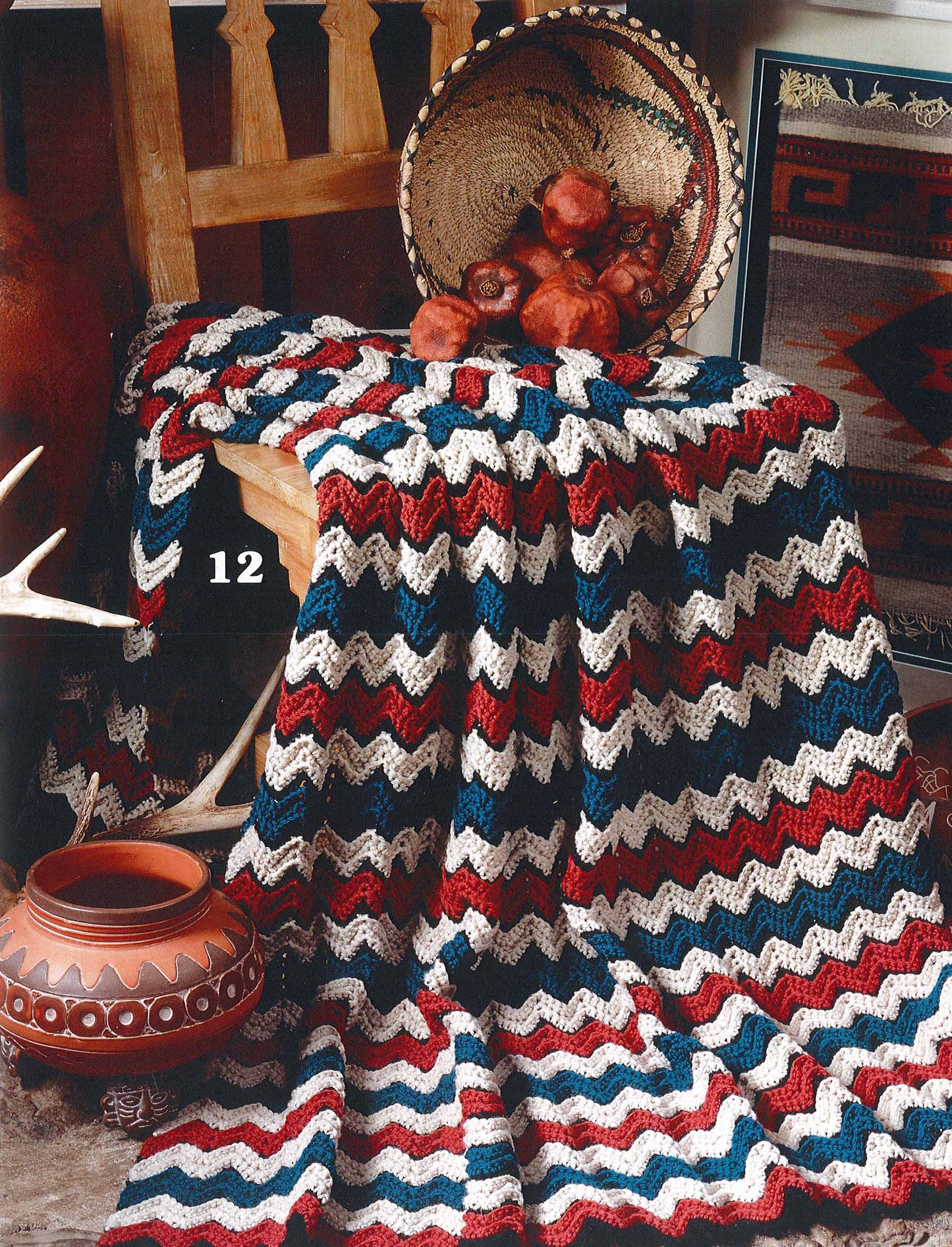 The Leisure Arts "Rippling Effects—16 Afghan Designs to Add to Your Home Decor" pattern is shown draped over a wooden chair beside southwestern pottery, with a woven basket of pomegranates on the seat and a patterned rug nearby.