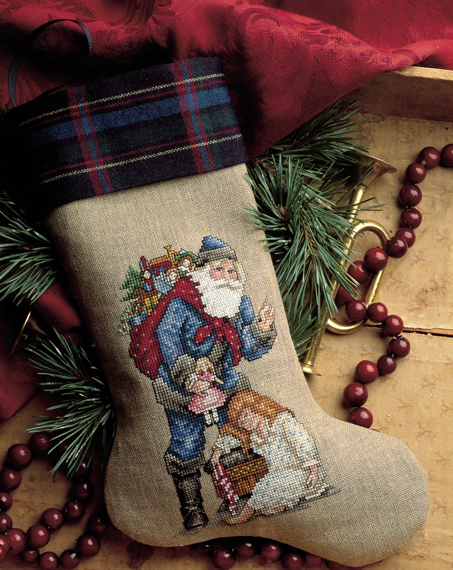 Santa's Great Book of Cross Stitch by Leisure Arts features festive patterns like Santa with toys and children, framed by pine branches and red accents—a perfect way to celebrate cherished holiday traditions.
