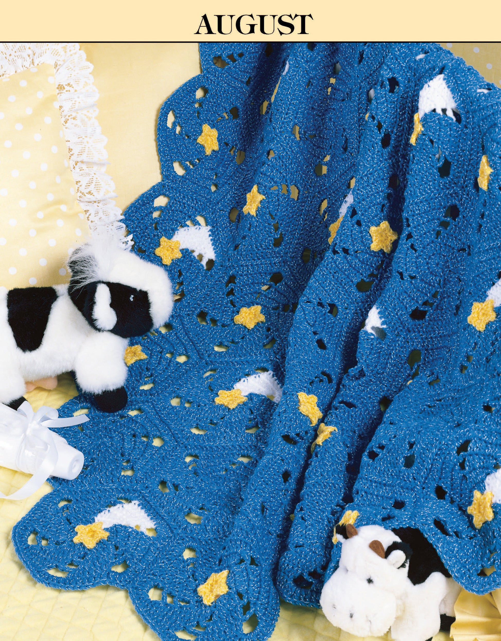 A blue crocheted blanket with yellow stars and white clouds, inspired by “August” from Leisure Arts’ A Year of Baby Afghans, Book 2, drapes over a yellow bed with stuffed cows and a lace-trimmed pillow—perfect for beginners.
