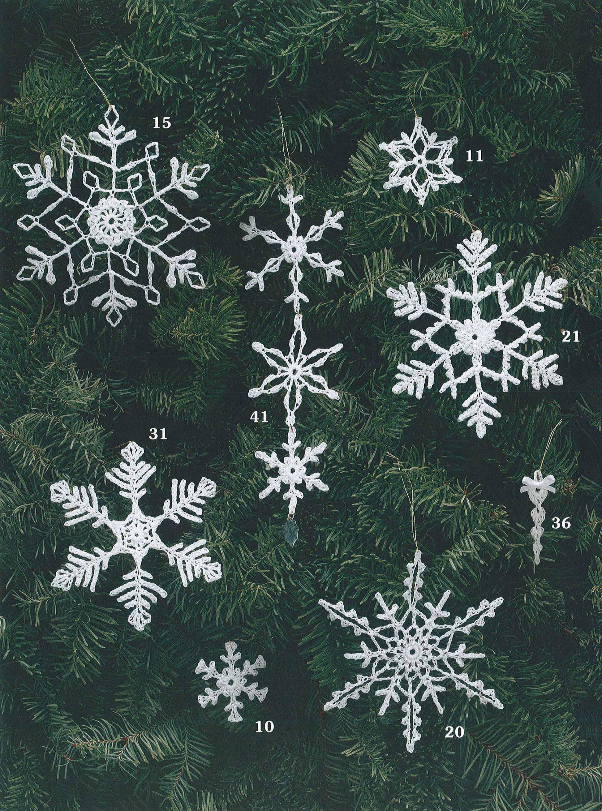 Seven unique white crocheted snowflake ornaments from the "White Christmas in Thread Crochet" collection by Leisure Arts hang on pine branches, each labeled with a small number from 10 to 41—ideal for garlands or tree toppers.