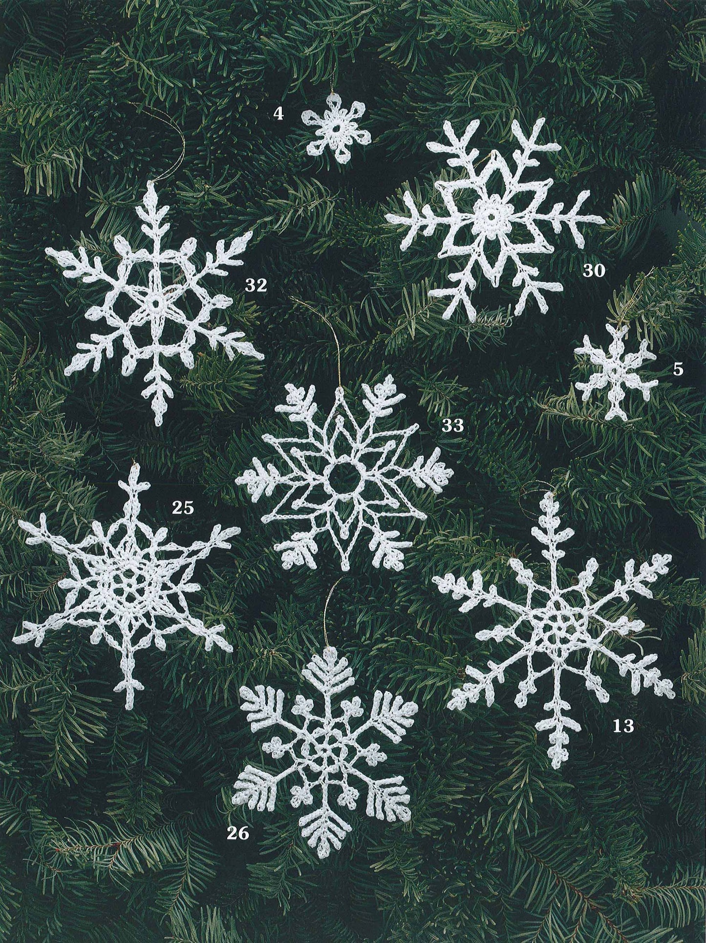 Seven uniquely patterned, numbered snowflake ornaments from "White Christmas in Thread Crochet" by Leisure Arts are shown on a green tree. Two small, numbered snowflakes add charm—ideal as ornaments or garlands.