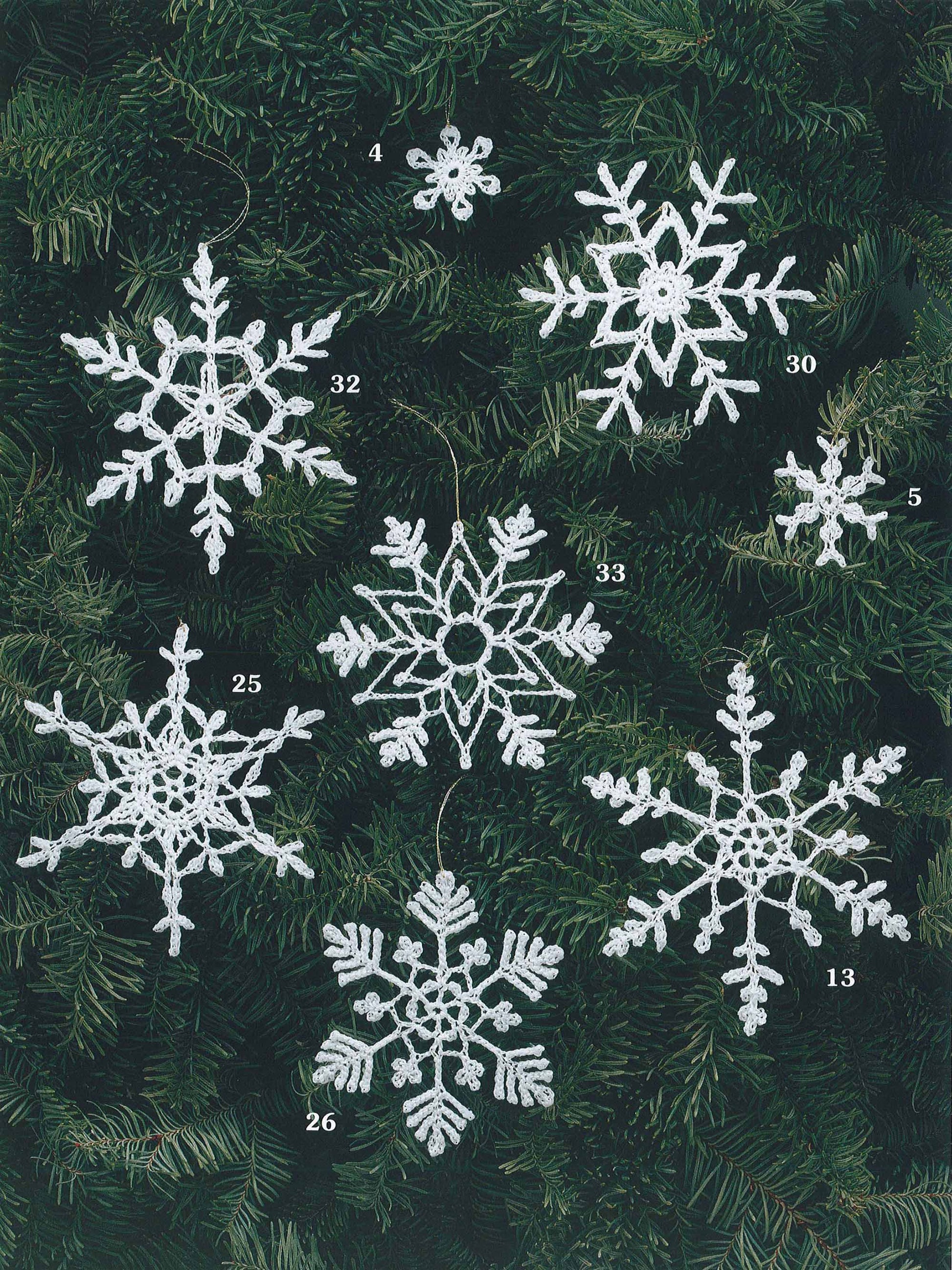 Seven uniquely patterned, numbered snowflake ornaments from "White Christmas in Thread Crochet" by Leisure Arts are shown on a green tree. Two small, numbered snowflakes add charm—ideal as ornaments or garlands.
