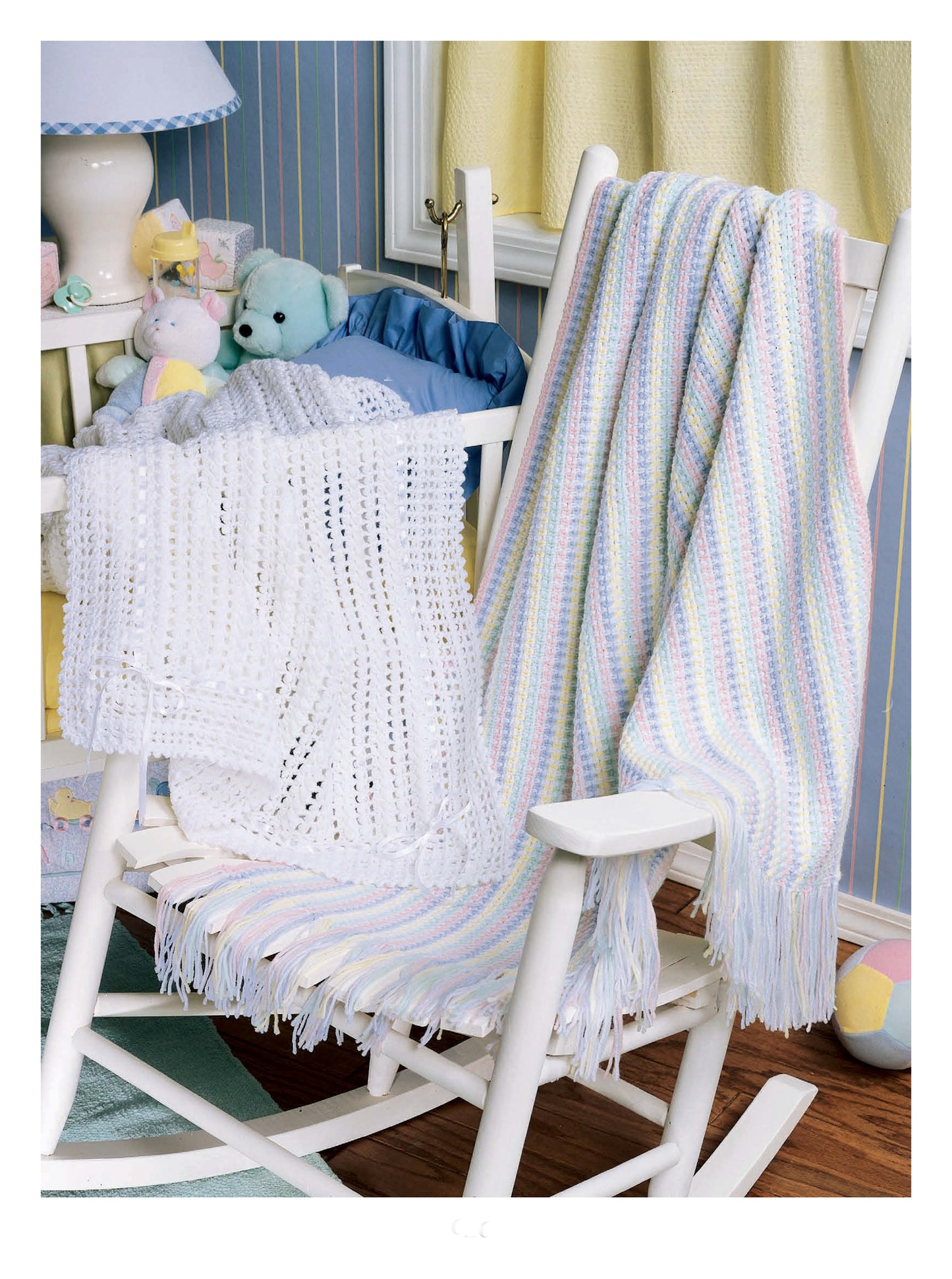 A white wooden rocking chair with soft toys in a cozy nursery displays the "Best of Terry Kimbrough Baby Afghans" by Leisure Arts, perfect for highlighting heirloom baby wraps and classic crochet designs.