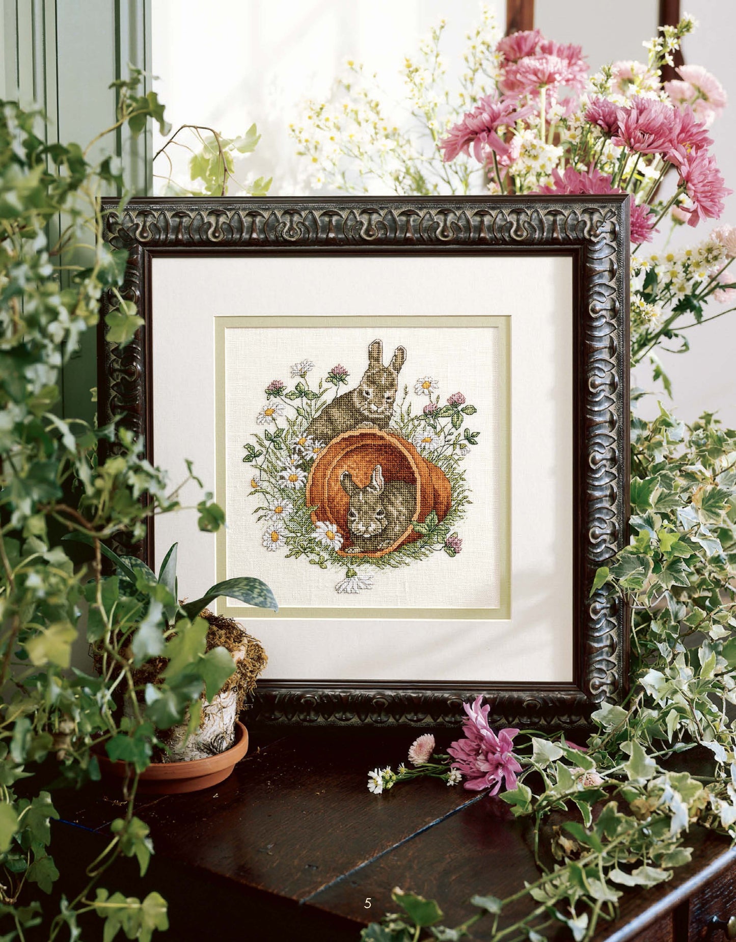 Something for Every Season by Leisure Arts offers 56 cross stitch designs as a digital download, featuring motifs like rabbits in a garden with pink flowers and green plants—ideal for holiday patterns or creative inspiration.