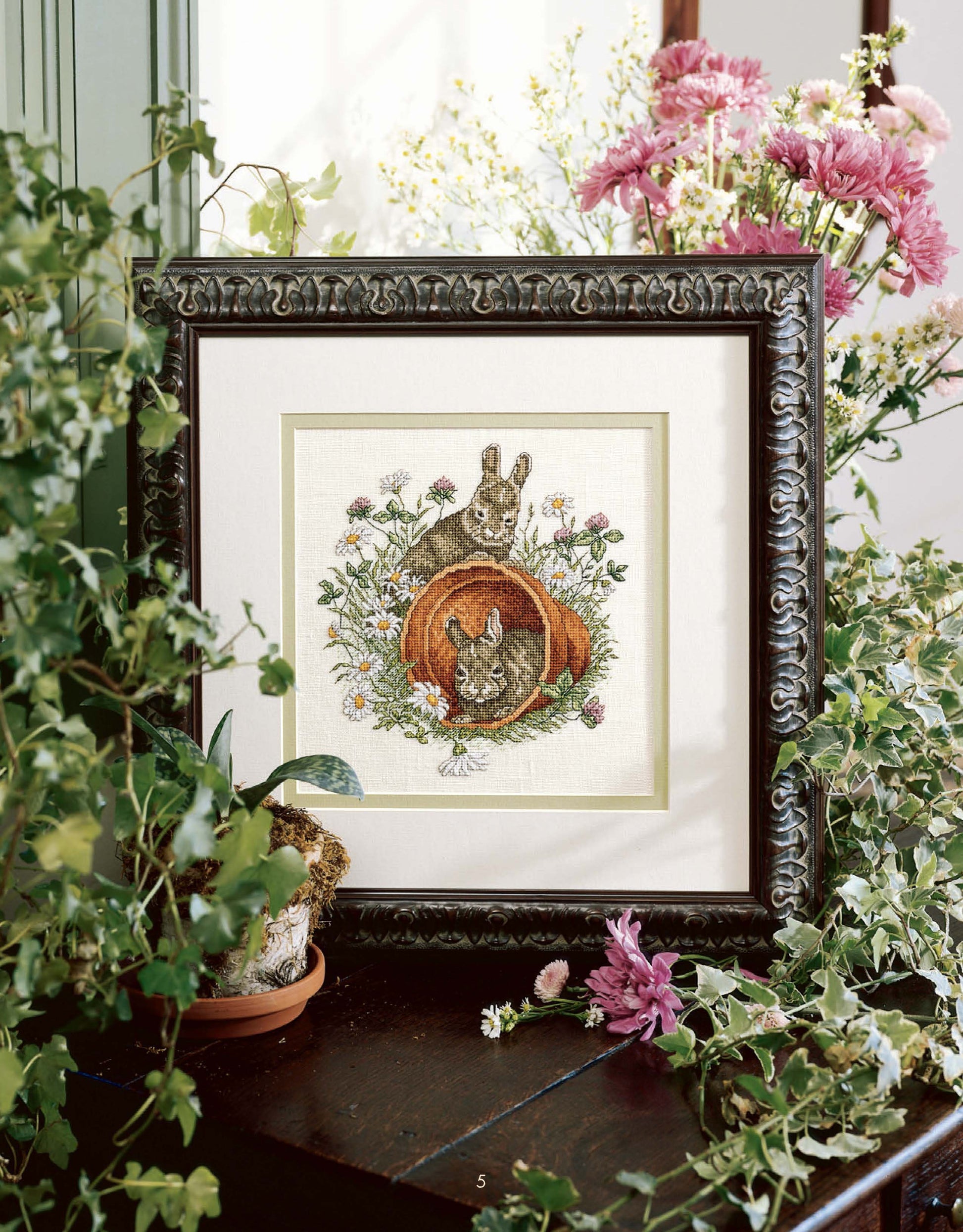 Something for Every Season by Leisure Arts offers 56 cross stitch designs as a digital download, featuring motifs like rabbits in a garden with pink flowers and green plants—ideal for holiday patterns or creative inspiration.