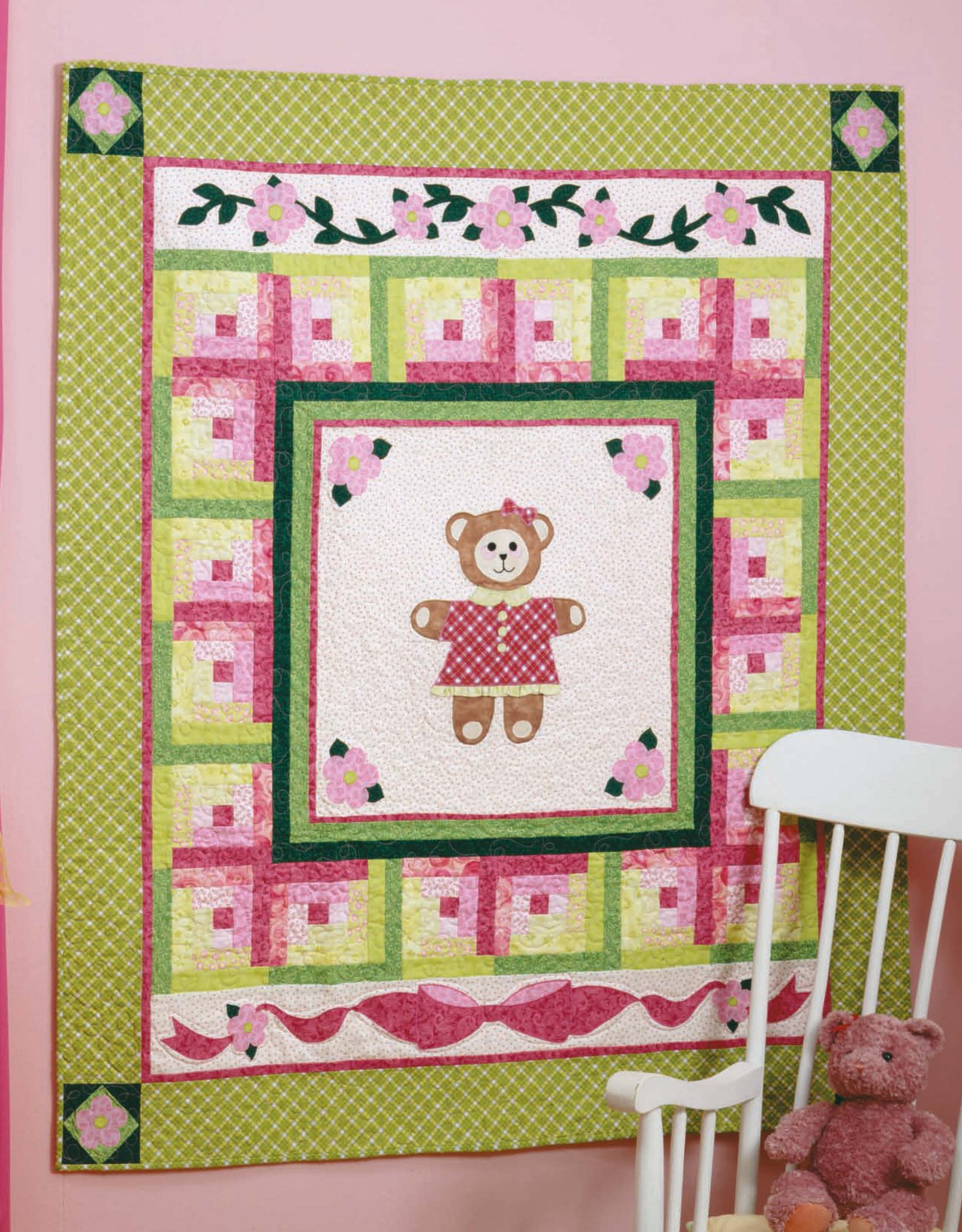 The Tadpole Quilts for Baby by Leisure Arts hangs on a pink wall above a white chair with a teddy bear, featuring a central teddy motif, pink, green, and yellow patchwork, floral accents, and easy-to-piece blocks.