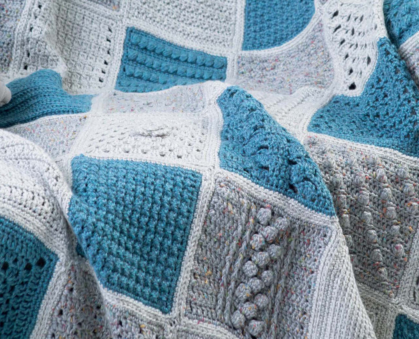 A close-up of textured blue, grey, and speckled white crochet squares—perfect for anyone using the "Easy to Crochet Pattern Stitches Digital Download" by Leisure Arts for afghan inspiration or mix-and-match block projects.