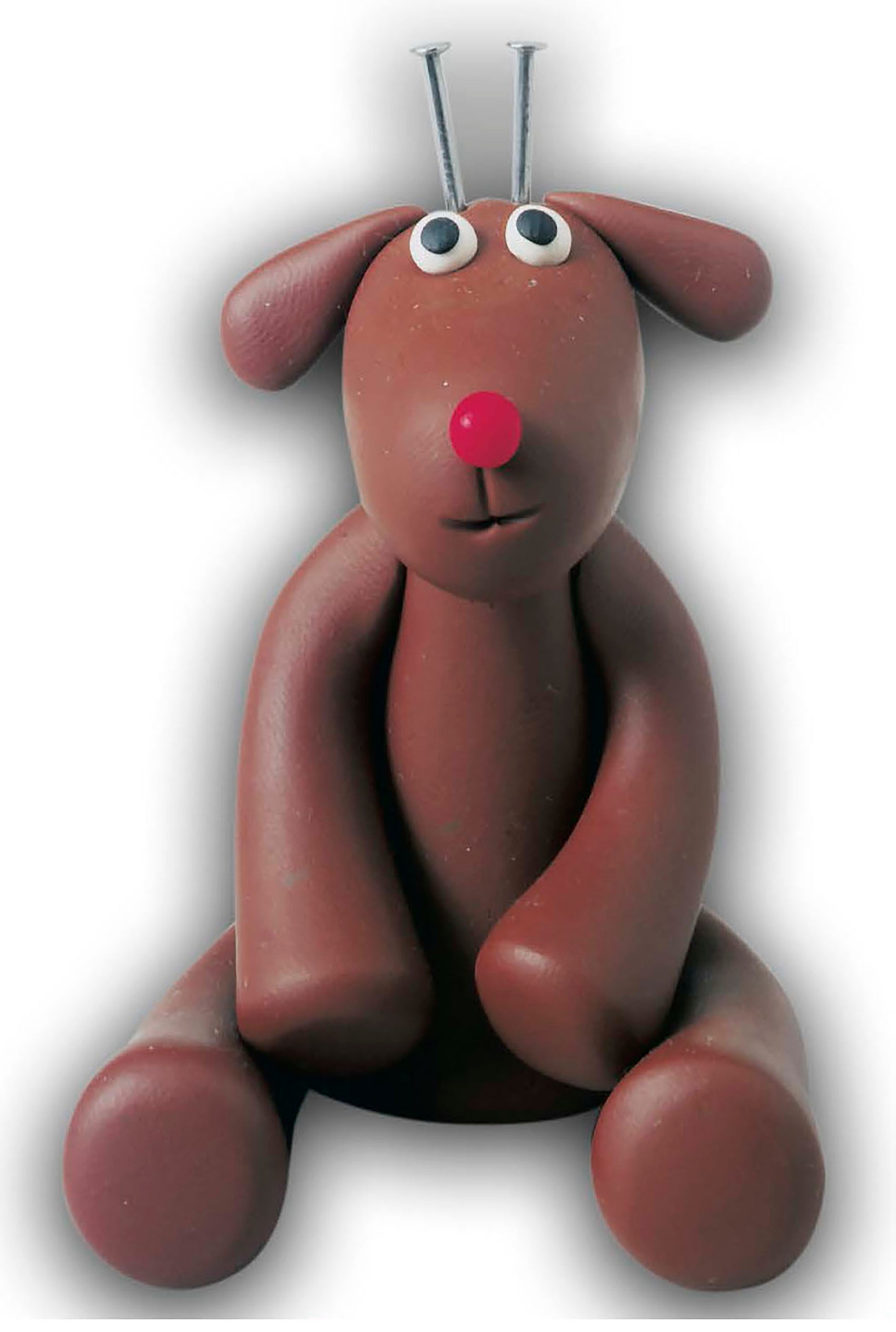 A brown clay dog figurine with big eyes, a red nose, and floppy ears sits upright—get inspired for your own creations with the "I Can't Believe I'm Sculpting Clay Figures" digital download by Leisure Arts.