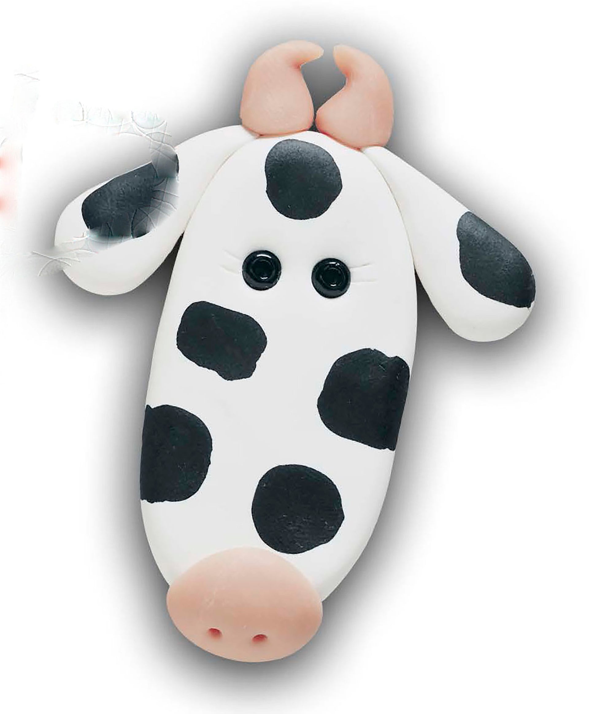 A cartoonish cow face clay figurine—black spots, button eyes, pink nostrils and horns—is shown on a white background. Create it with Leisure Arts' "I Can't Believe I'm Sculpting Clay Figures Digital Download" for beginners or step-by-step sculptors.