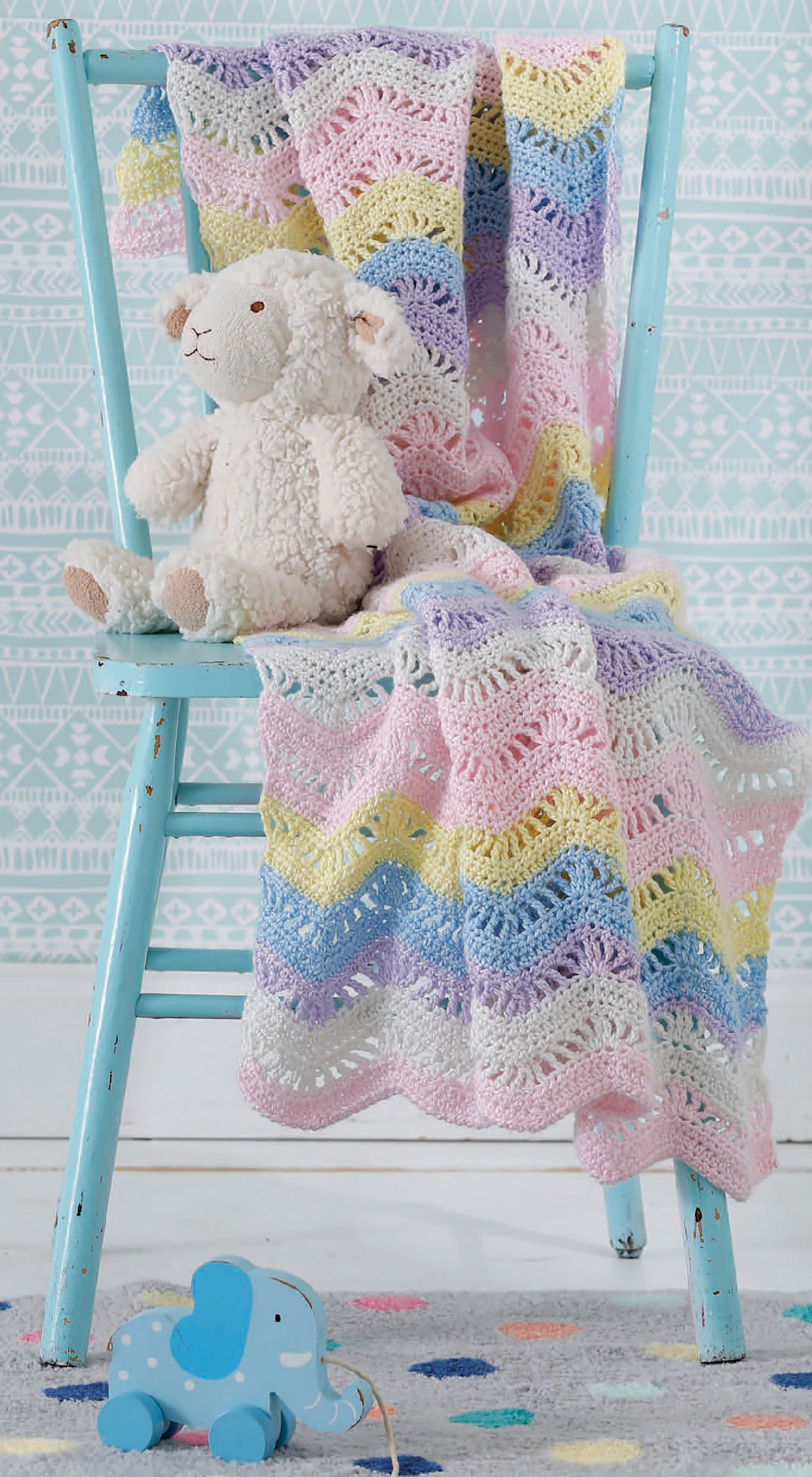 A pastel crochet baby blanket drapes over a blue chair with a plush sheep, while a pull-toy elephant sits nearby. Create your own cozy nursery with Our Best Baby Afghans Digital Download by Leisure Arts—perfect for inspiring baby blanket patterns.
