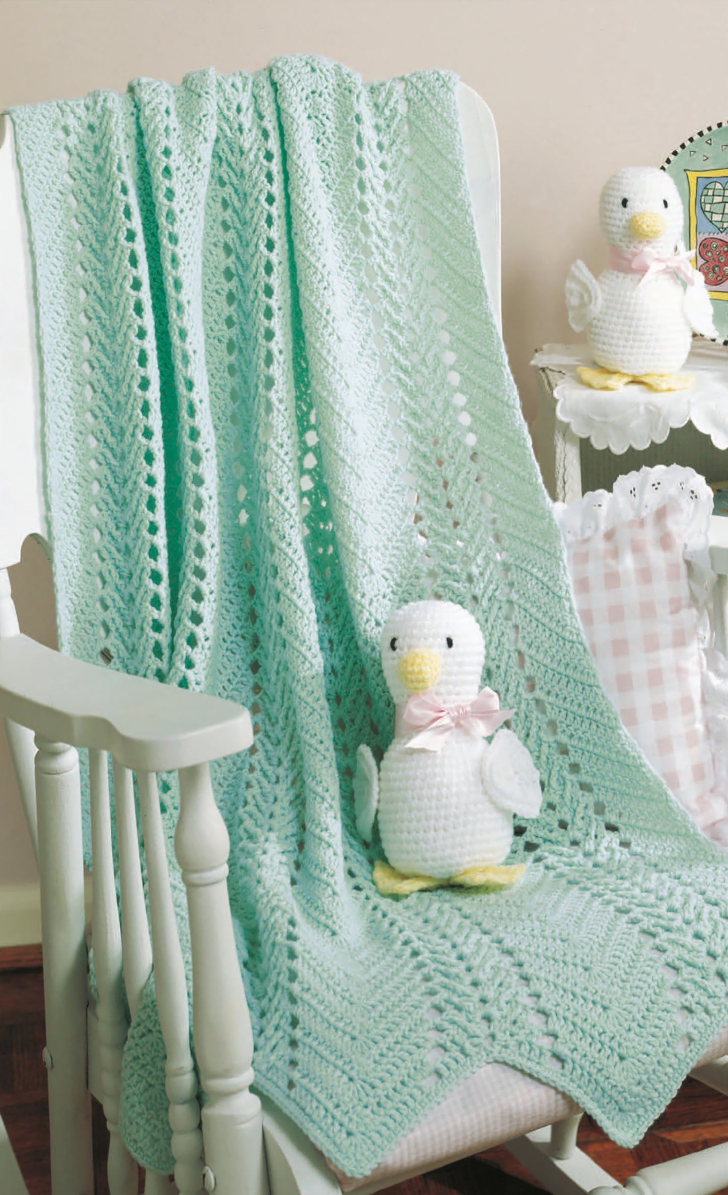 The Just Ducky Baby Afghans Digital Download by Leisure Arts features a mint green crocheted blanket and two white crocheted duck toys with yellow beaks, feet, and pastel ribbons—charming nursery gifts.