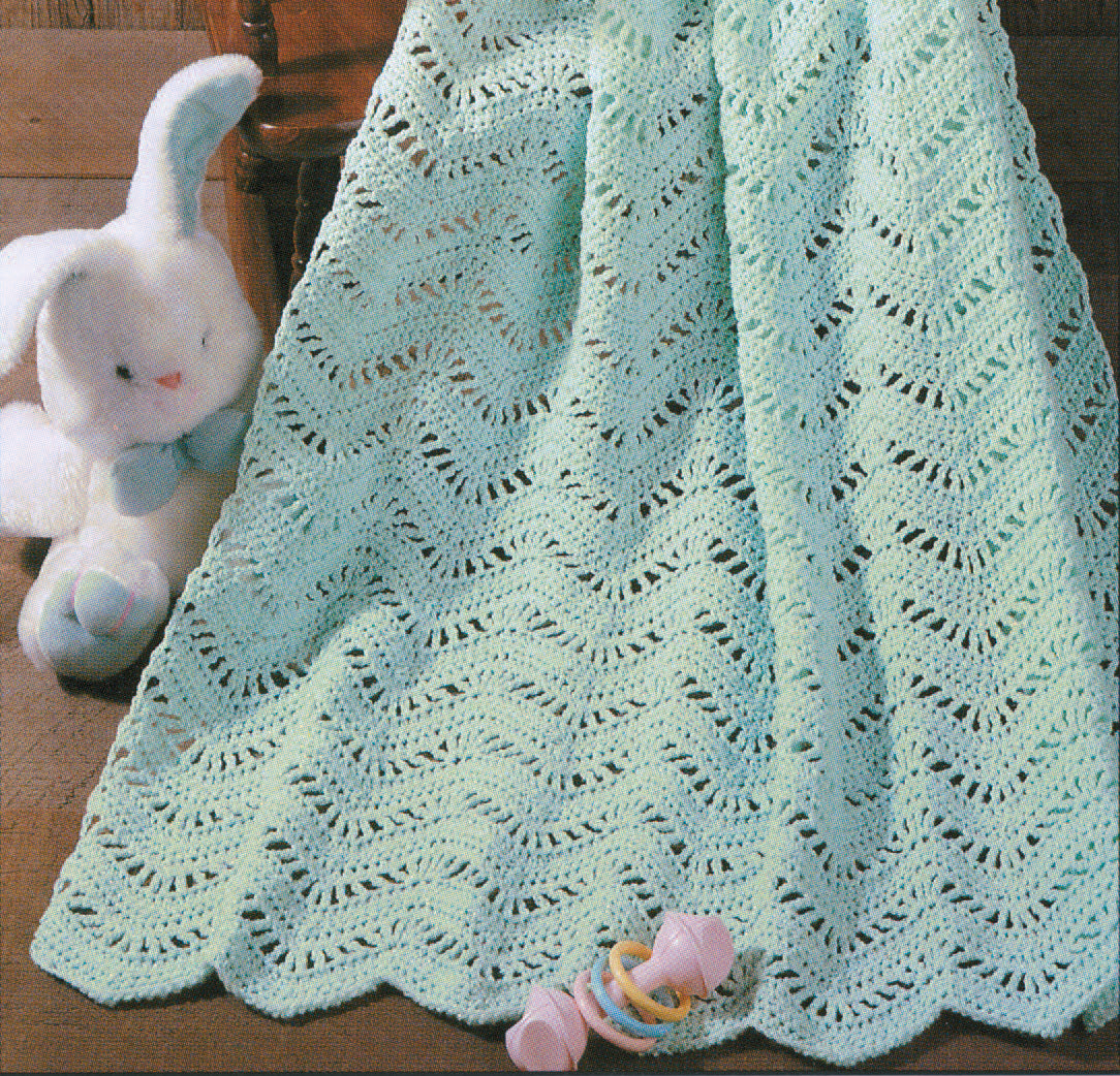 The Snuggle-Up Baby Afghans digital download by Leisure Arts offers 8 beginner-friendly crochet patterns, including a soft mint green wavy design, shown draped on wood with a white bunny and colorful rattle nearby.