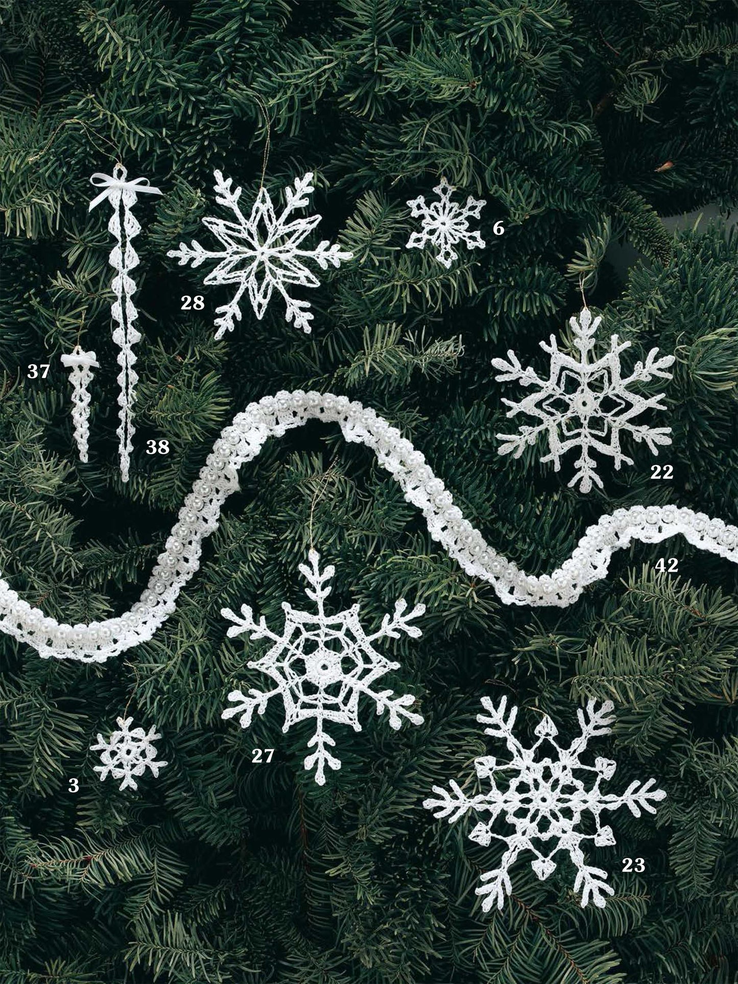 Leisure Arts' White Christmas in Thread Crochet Digital Download features numbered white snowflake, icicle ornaments, and a wavy garland displayed on pine branches—perfect for holiday decor.