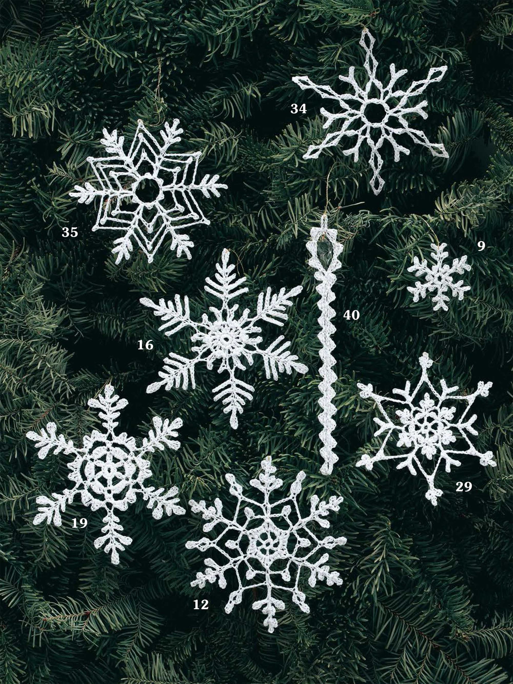 Eight crocheted white ornaments (numbers 9, 12, 16, 19, 29, 34, 35, and 40) from the Leisure Arts White Christmas in Thread Crochet Digital Download hang on pine branches—perfect festive holiday decor!.