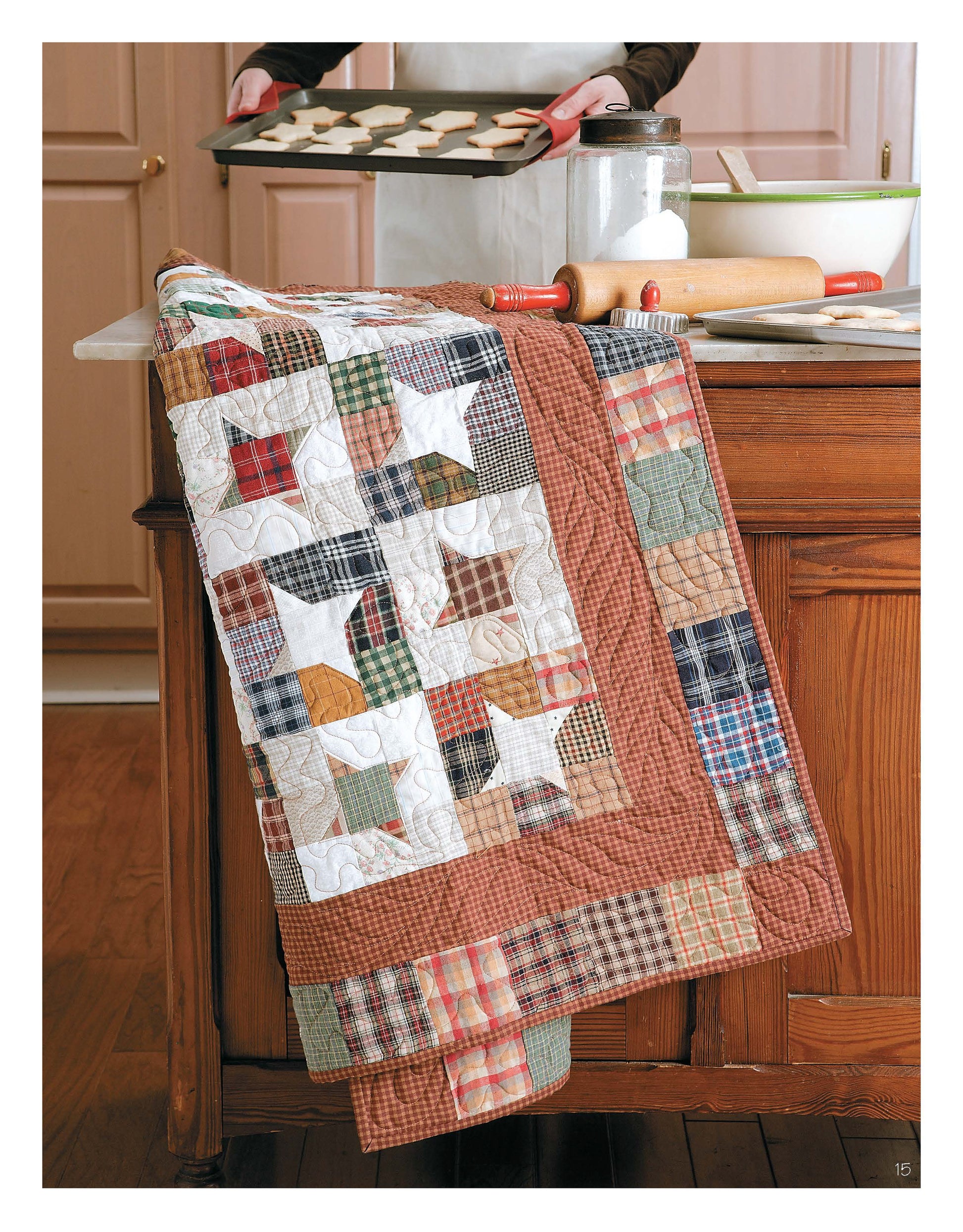 A vibrant quilt from the "Slash Your Stash Quilts Digital Download" by Leisure Arts drapes over a kitchen counter with baking supplies, while someone in the background prepares to bake cookies.