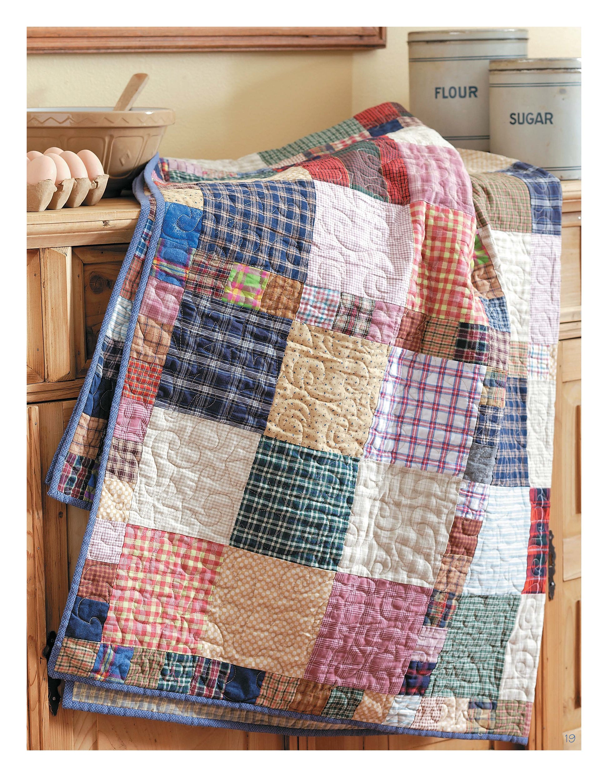 The Slash Your Stash Quilts Digital Download by Leisure Arts features a vibrant quilt made with speedy piecing, displayed atop a wooden cabinet beside vintage “flour” and “sugar” tins and a bowl of eggs for a charming kitchen touch.