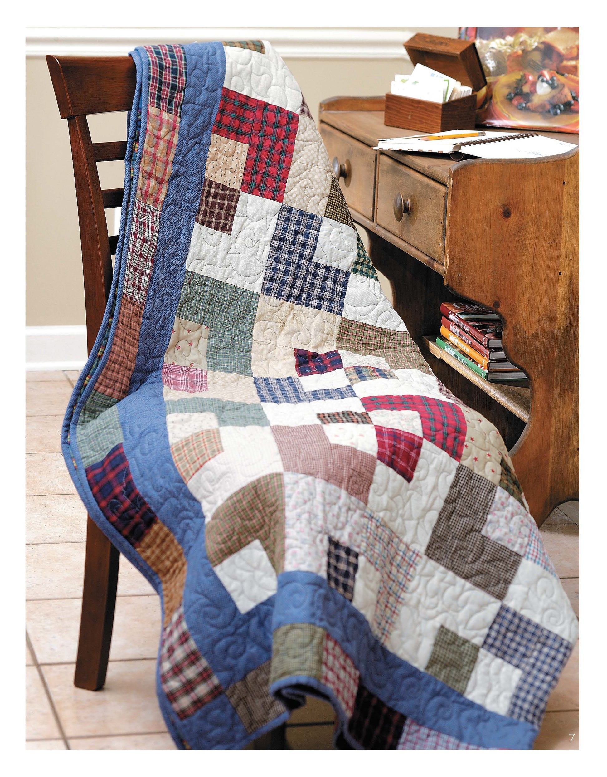 A cozy room features a wooden chair draped with a quilt inspired by Slash Your Stash Quilts Digital Download from Leisure Arts, its vibrant patchwork and fast piecing design brightening the space beside a rustic desk.