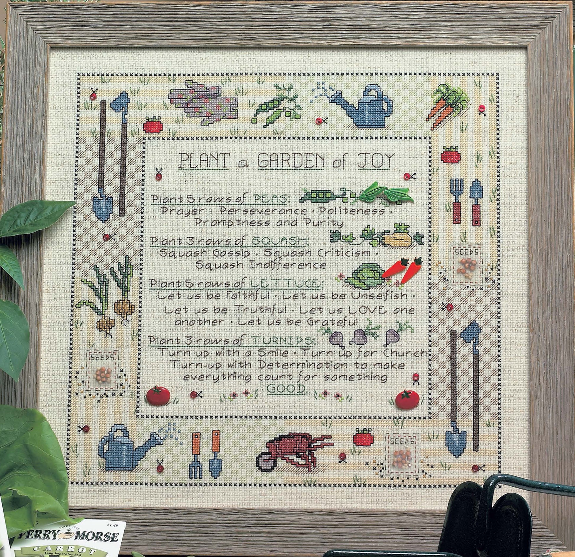 Framed "Life Tips from the Garden" cross stitch by Leisure Arts on Aida cloth, with vegetable puns, heirloom patterns, and a charming poem. Features gardening motifs and includes a Ferry-Morse carrot seed packet in the corner.