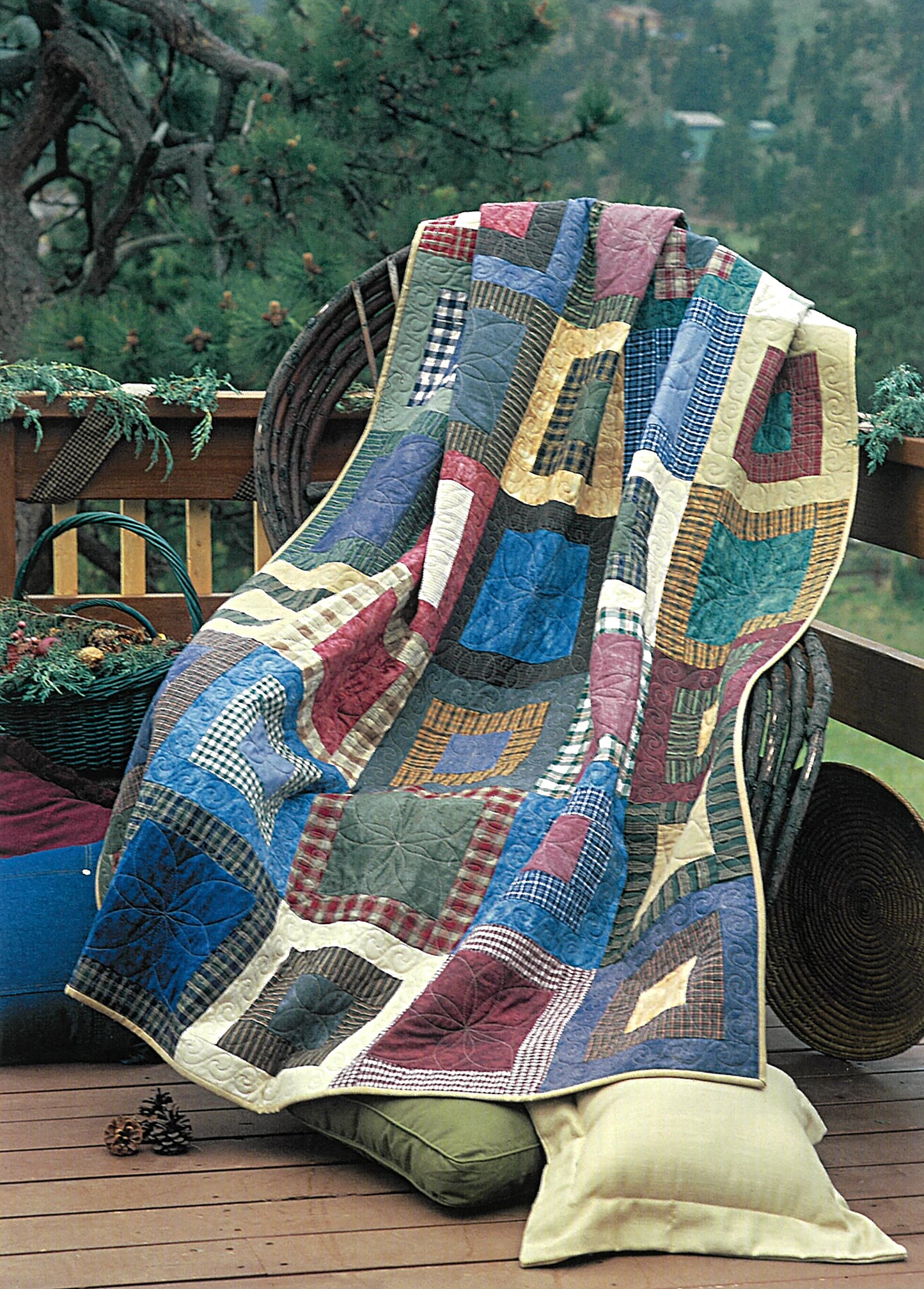 A vibrant scrap quilt from Leisure Arts' Quick & Scrappy Quilts is draped over a wicker chair on a wooden deck, pine trees in the background. A yellow pillow sits beside the chair.