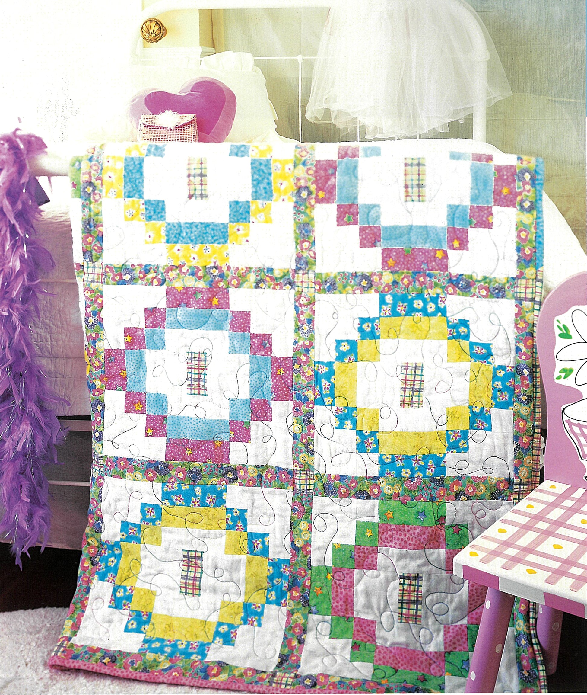The Quick & Scrappy Quilts by Leisure Arts features vibrant patchwork in pink, blue, yellow, and green on a white metal bed with a heart pillow and purple feather boa nearby; a pink chair appears on the right.