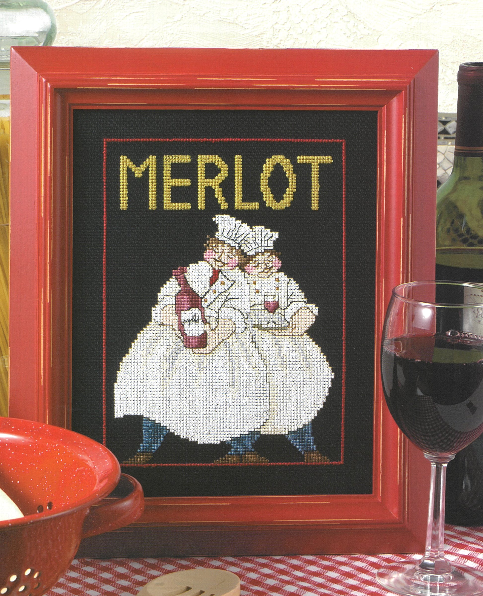 Leisure Arts' "French Chefs—4 Cross Stitch Designs" features chefs with wine bottles and “MERLOT” above, plus a red wine glass on a checkered cloth—a stylish kitchen decor piece.